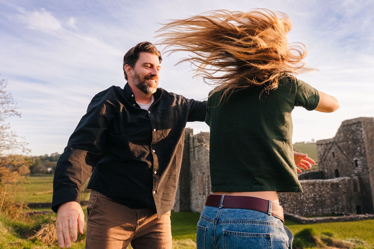 A couple dancing together outdoors with hair blowing in the wind against a cloudy sky. Photographer Ireland dublin