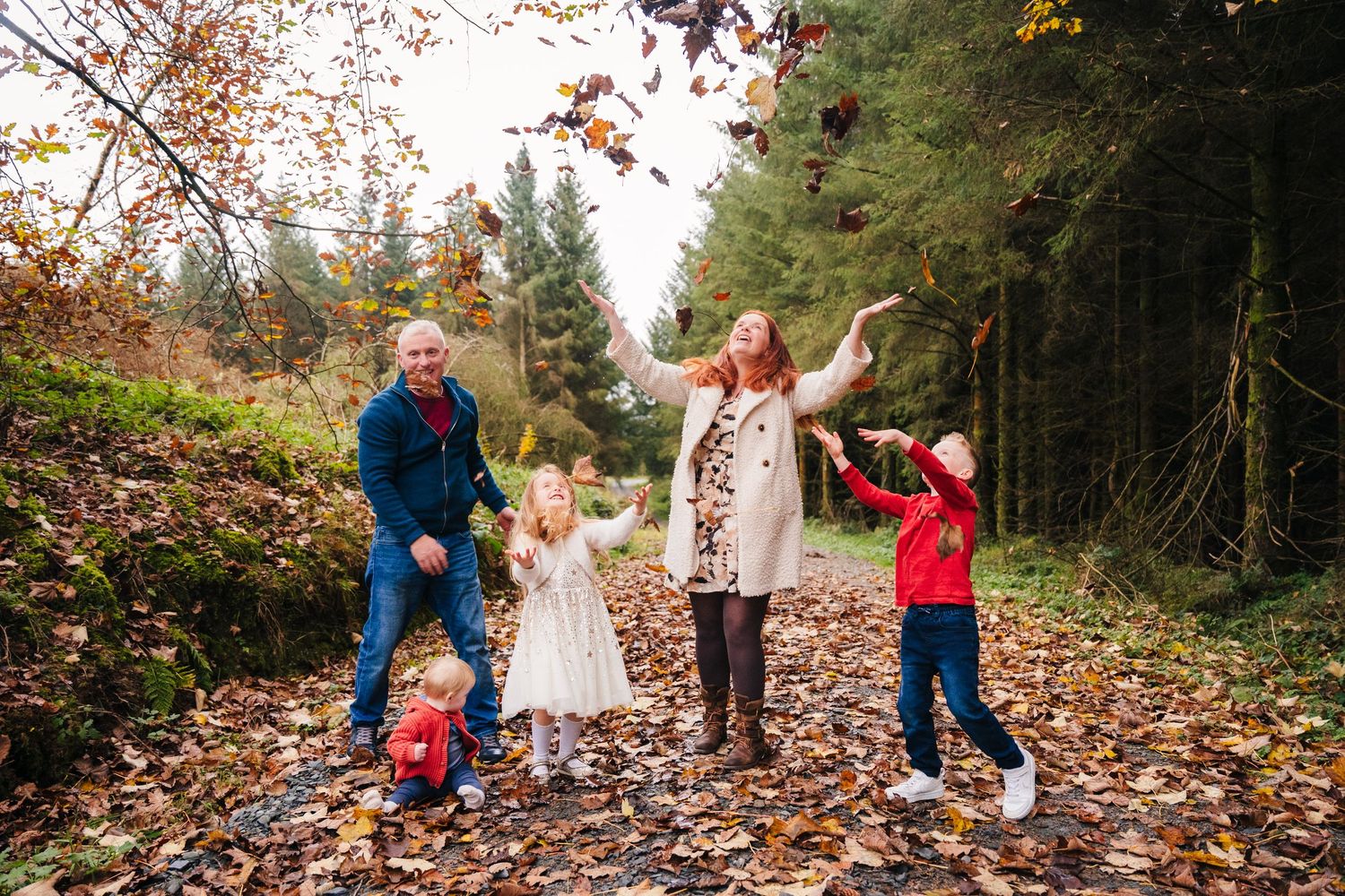 Family Photographer Dublin Ireland Family walking together on a leaf-covered path through a wooded area during fall season.