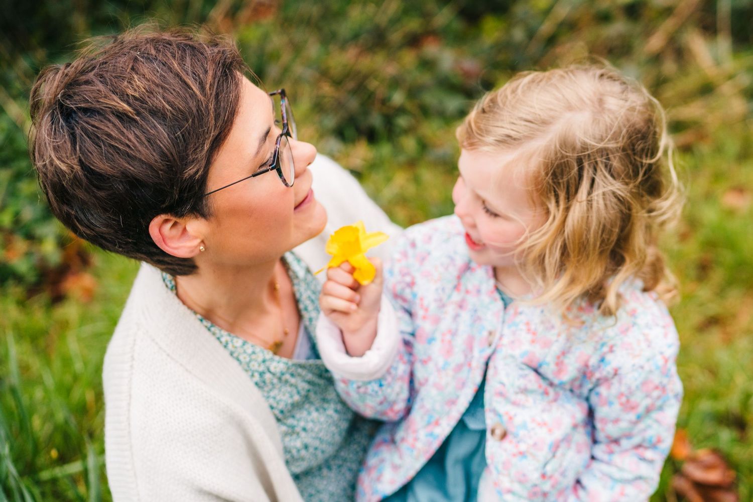 A parent and child share a sweet moment outdoors while holding a yellow dandelion flower in spring. Family photographer Dublin Ireland