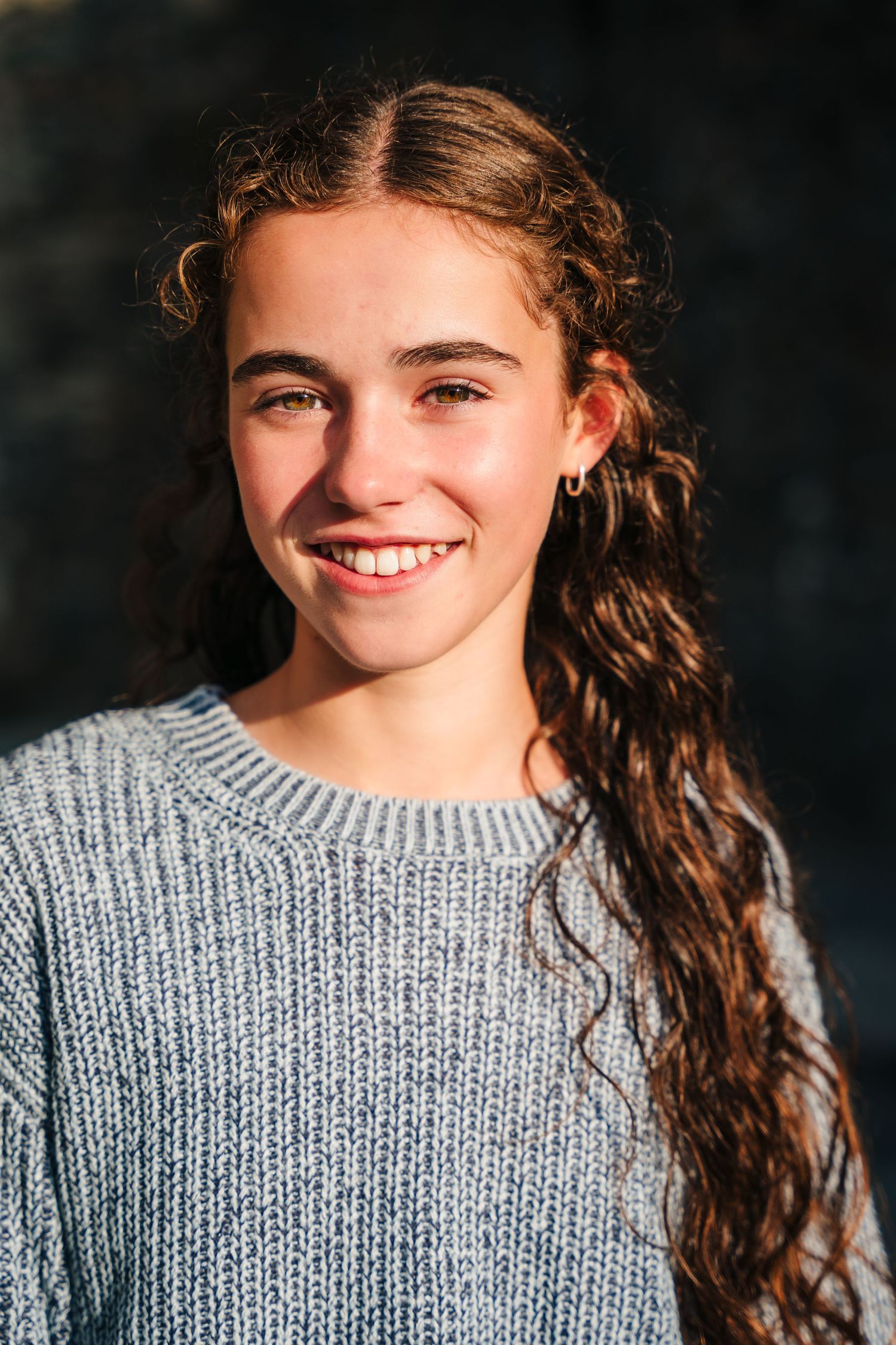 Family photographer IrelPortrait of someone wearing a cozy gray sweater on a dark background with warm sunlight illuminating their features.