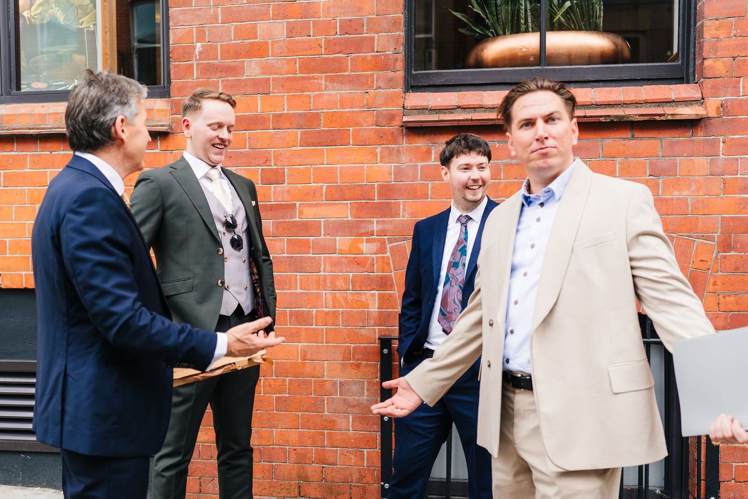 A group of formally dressed people chatting outside a brick building. PHOTOGRAPHER Dublin Ireland Wedding