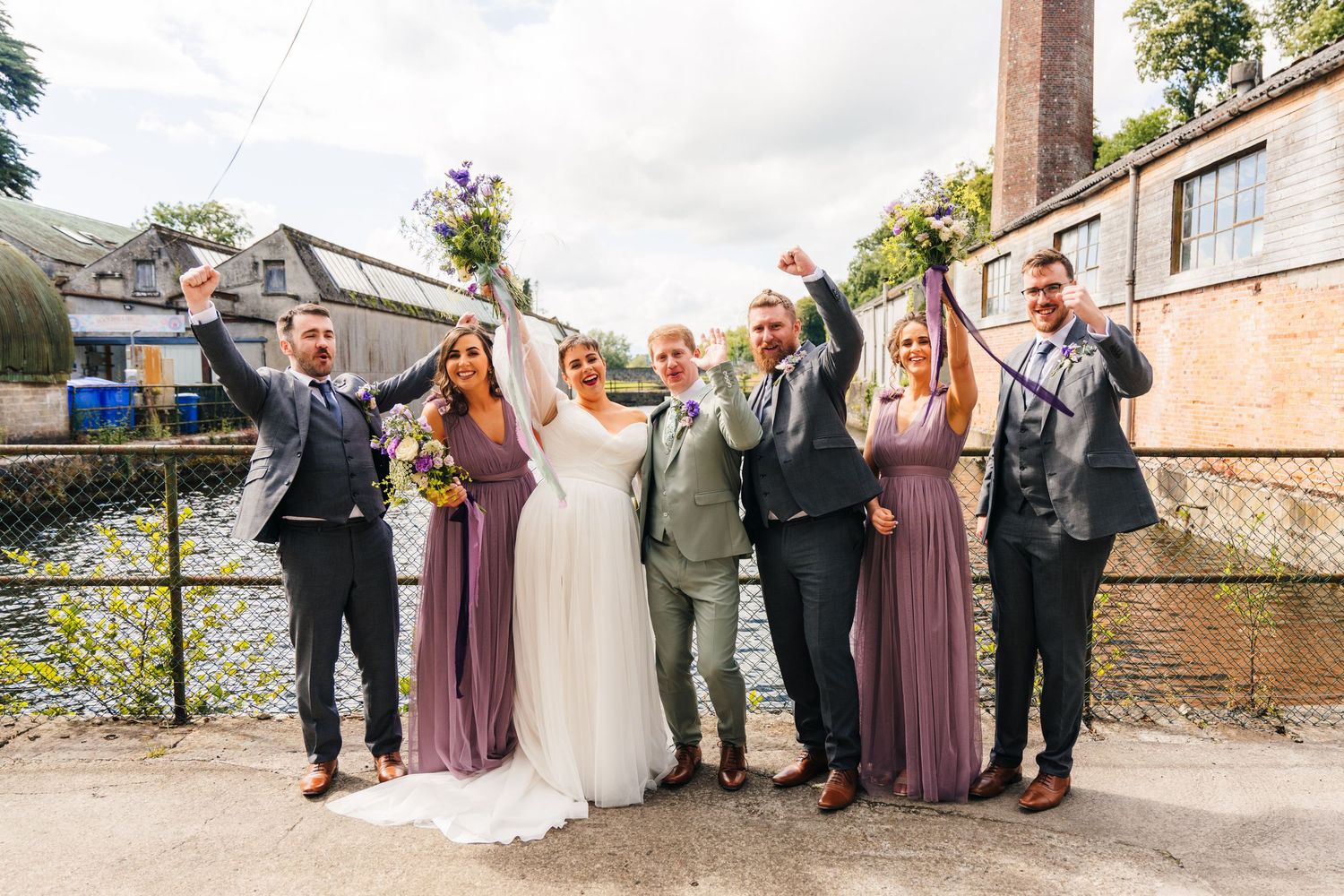 Millhouse slane wedding photographer dublin Wedding party and guests posing joyfully outside a historic building on a cloudy day.