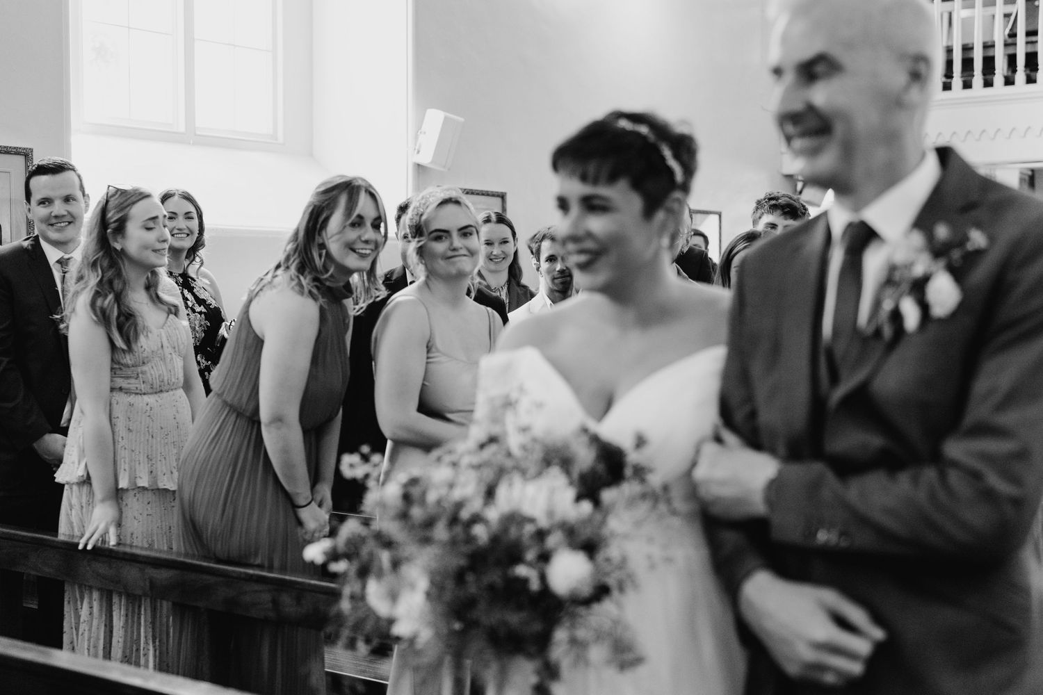 Millhouse slane wedding photographer dublin Black and white photo of wedding party sharing laughs during church ceremony.