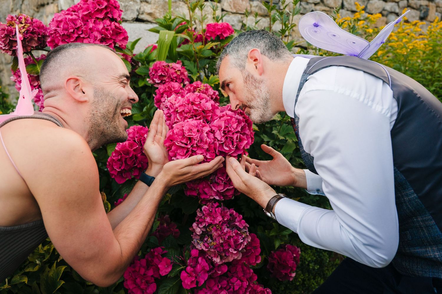 Two people smell bright pink flowers together in a garden setting. . Village Barn Tyrrellspass wedding photographer Ireland