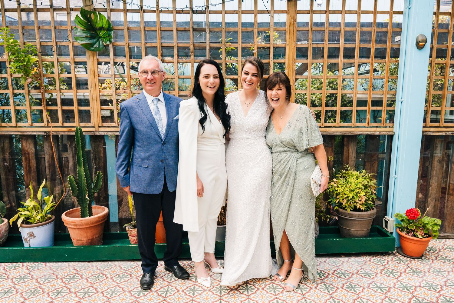 Small group poses together in front of a wooden lattice wall with plants. House Dublin Wedding Photographer