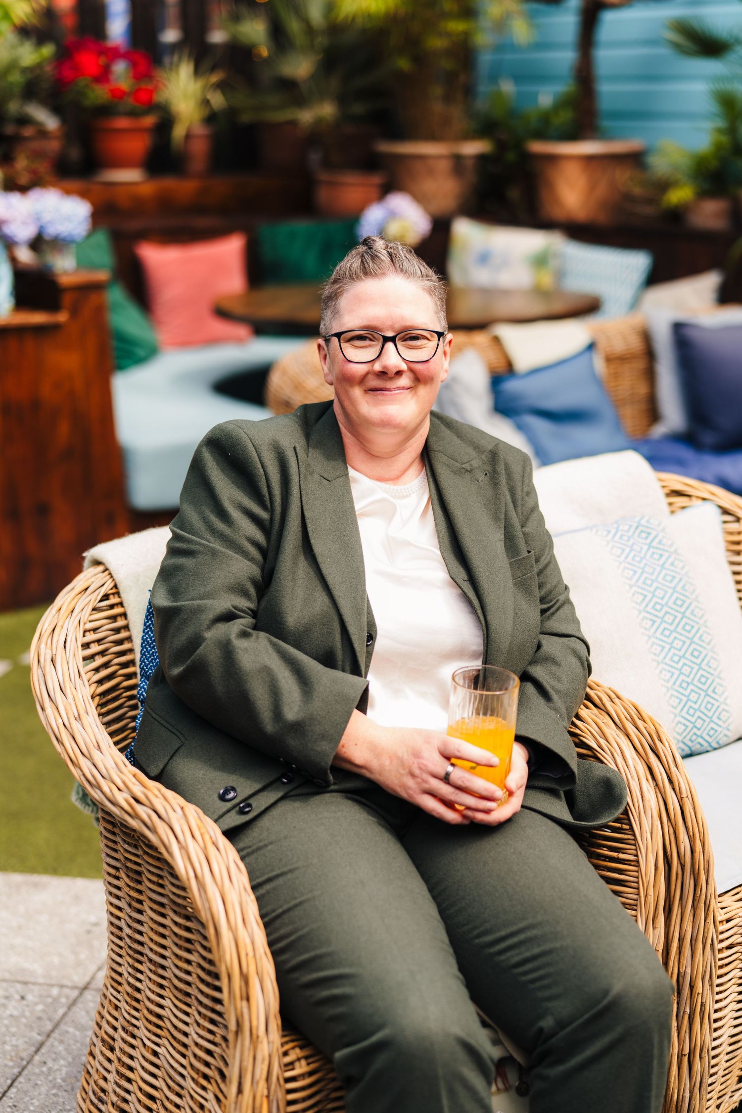 A person relaxes in a wicker chair on a patio with a glass of orange juice while wearing a green blazer and glasses. House Dublin Wedding Ph