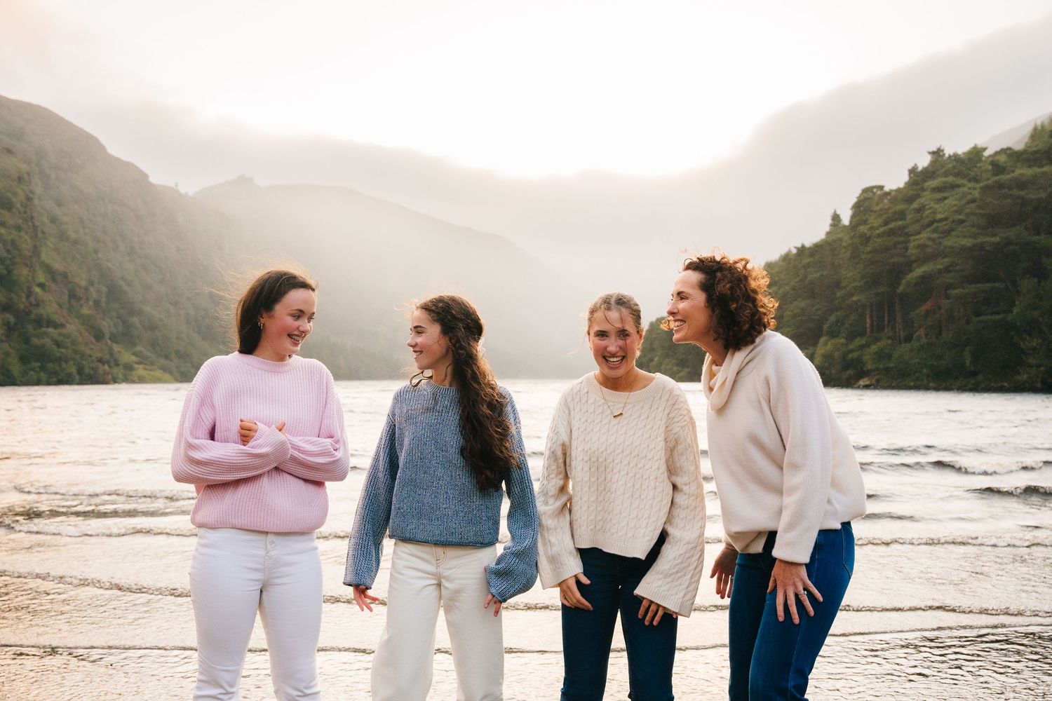 Family photographer Ireland Dublin Four friends share laughs together on a lakeside beach with mountain scenery in the background.