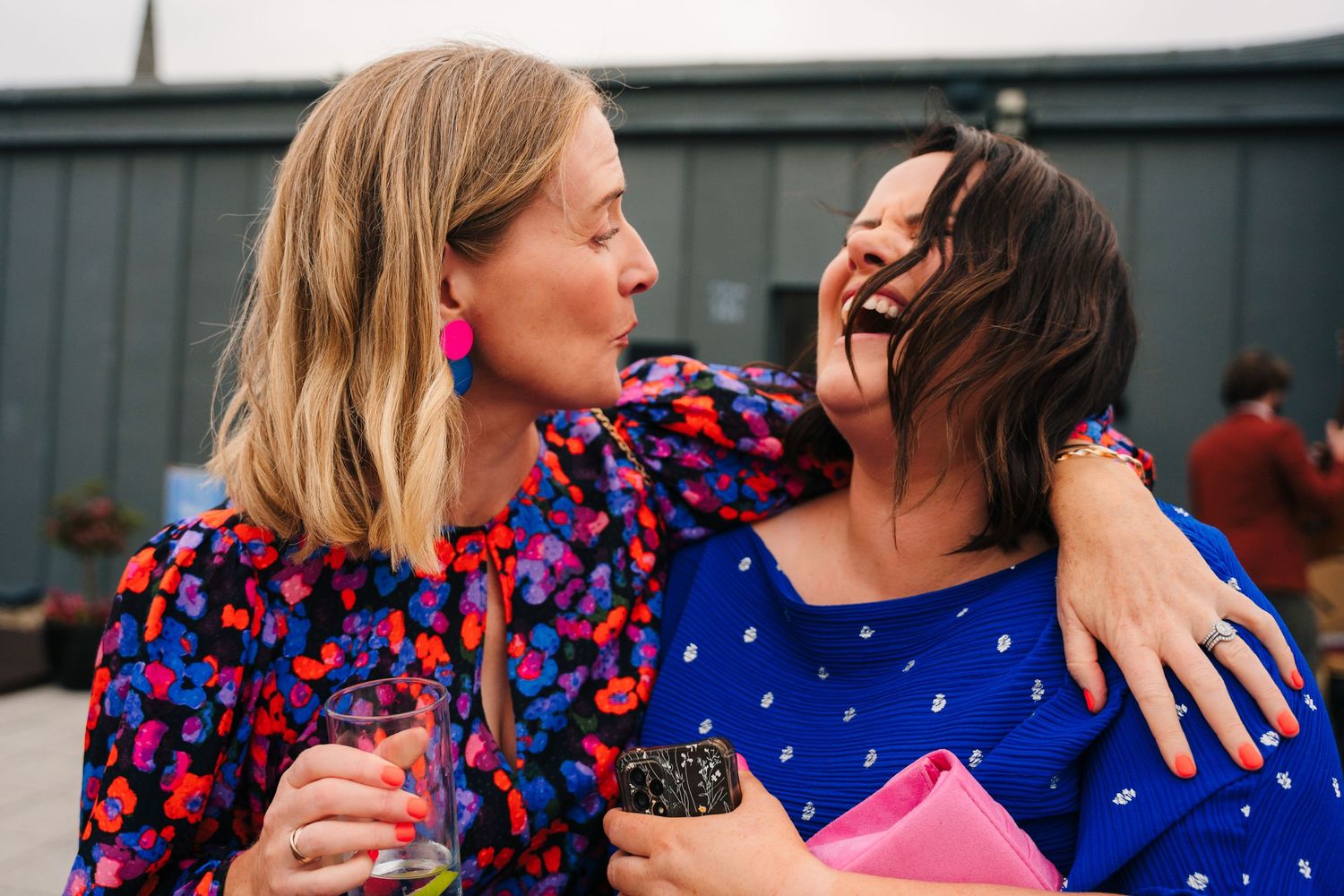 Friends embrace and laugh while wearing bright blue and floral dresses at outdoor gathering.Wedding Photography Trim Castle Ireland
