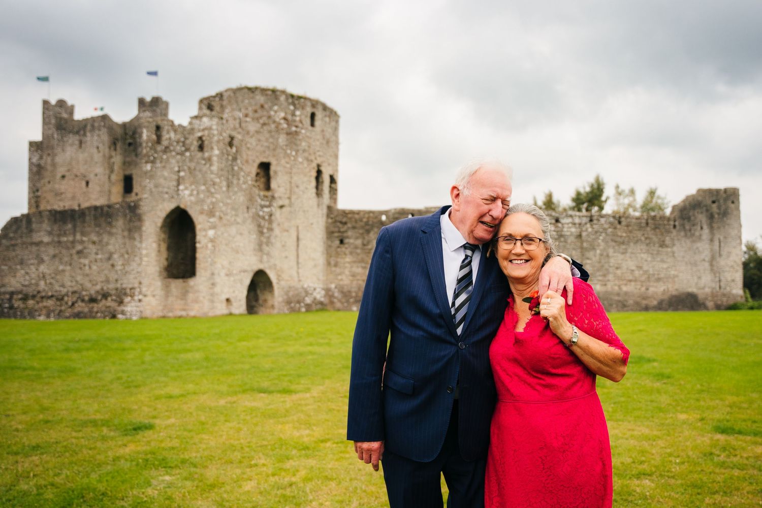 Happy couple posing together in front of a historic stone castle on a cloudy day. Wedding Photography Trim Castle Ireland