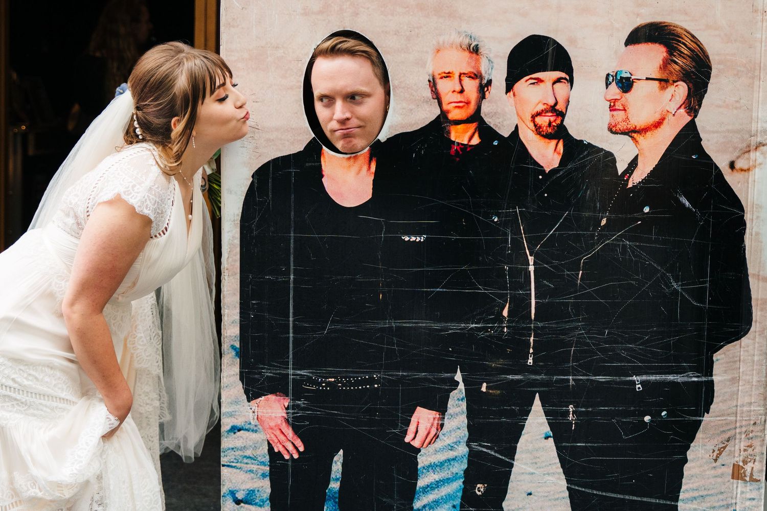 Bride in white dress poses playfully next to a large black and white U2 band poster. PHOTOGRAPHER Dublin Ireland Wedding