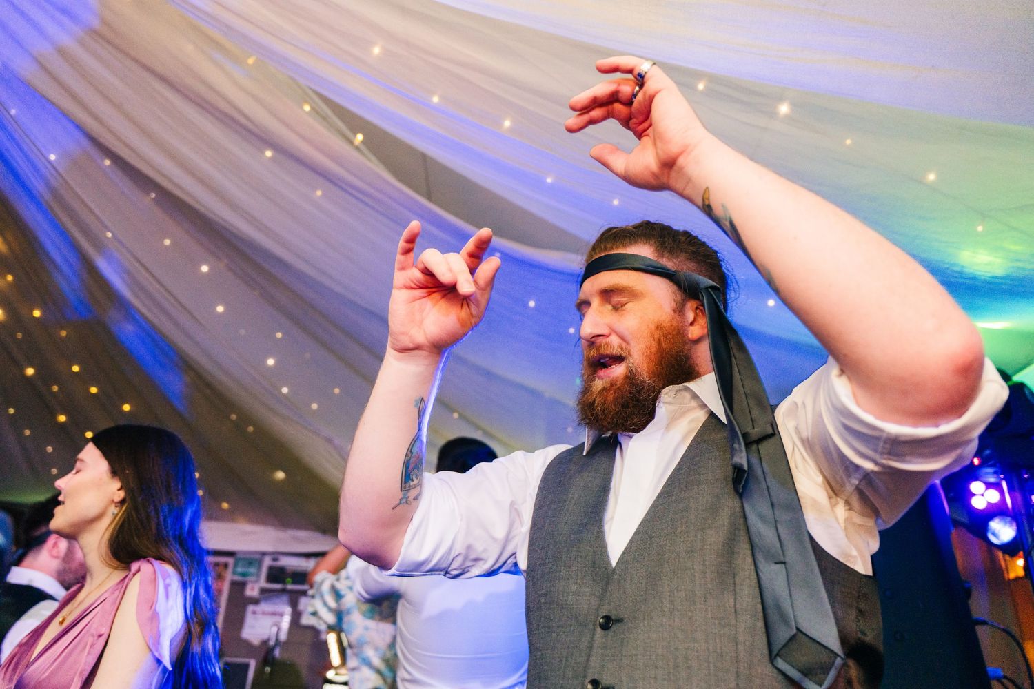 Millhouse slane wedding photographer dublin Wedding party celebrates with raised arms under blue lighting at evening reception.