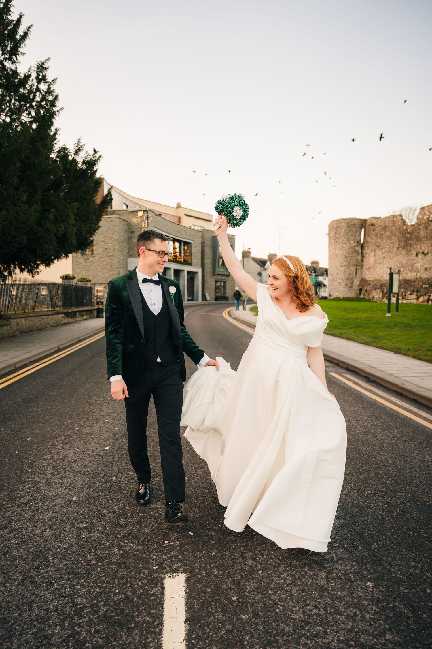 Bride and groom walking along a castle wall path while bride's dress flows in the wind.  Wedding PHOTOGRAPHER Trim Castle