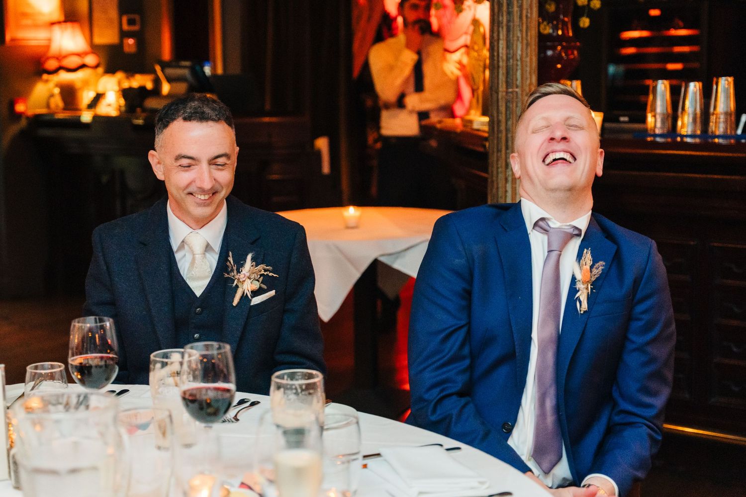 Two guests at a formal dinner share a laugh at a warmly lit restaurant table. Marco Pierre Dublin Wedding Photographer