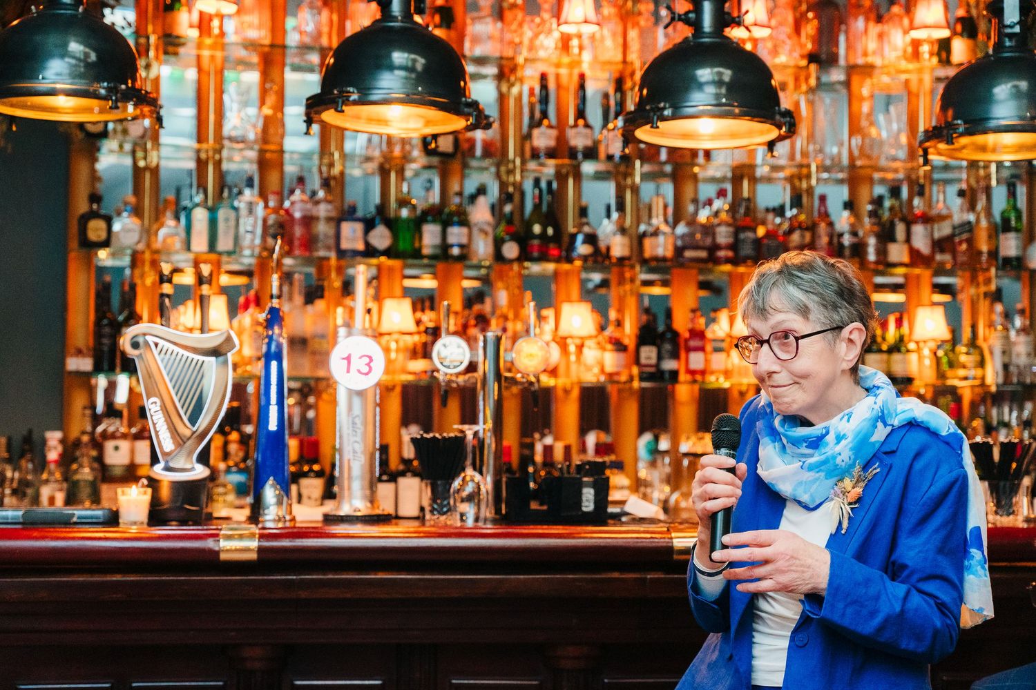 A bartender in blue serves drinks at a well-stocked bar with dramatic lighting. Marco Pierre Dublin Wedding Photographer