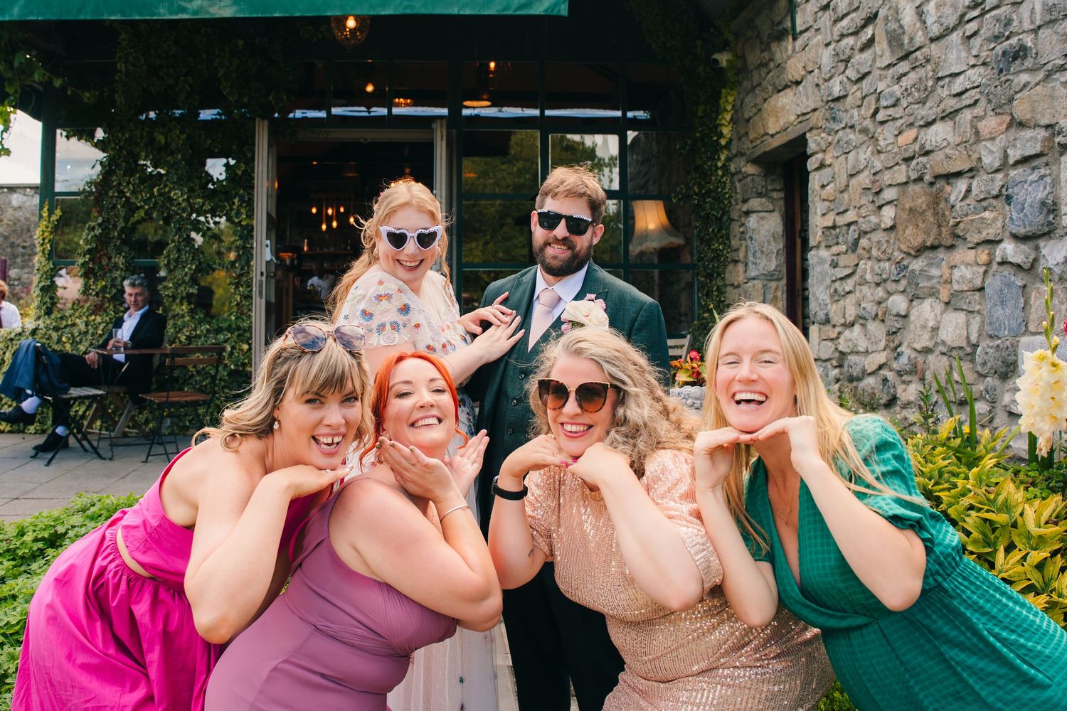 Candid photo strip showing wedding party members posing and making fun expressions outdoors by a stone wall. . Village Barn Tyrrellspass wed