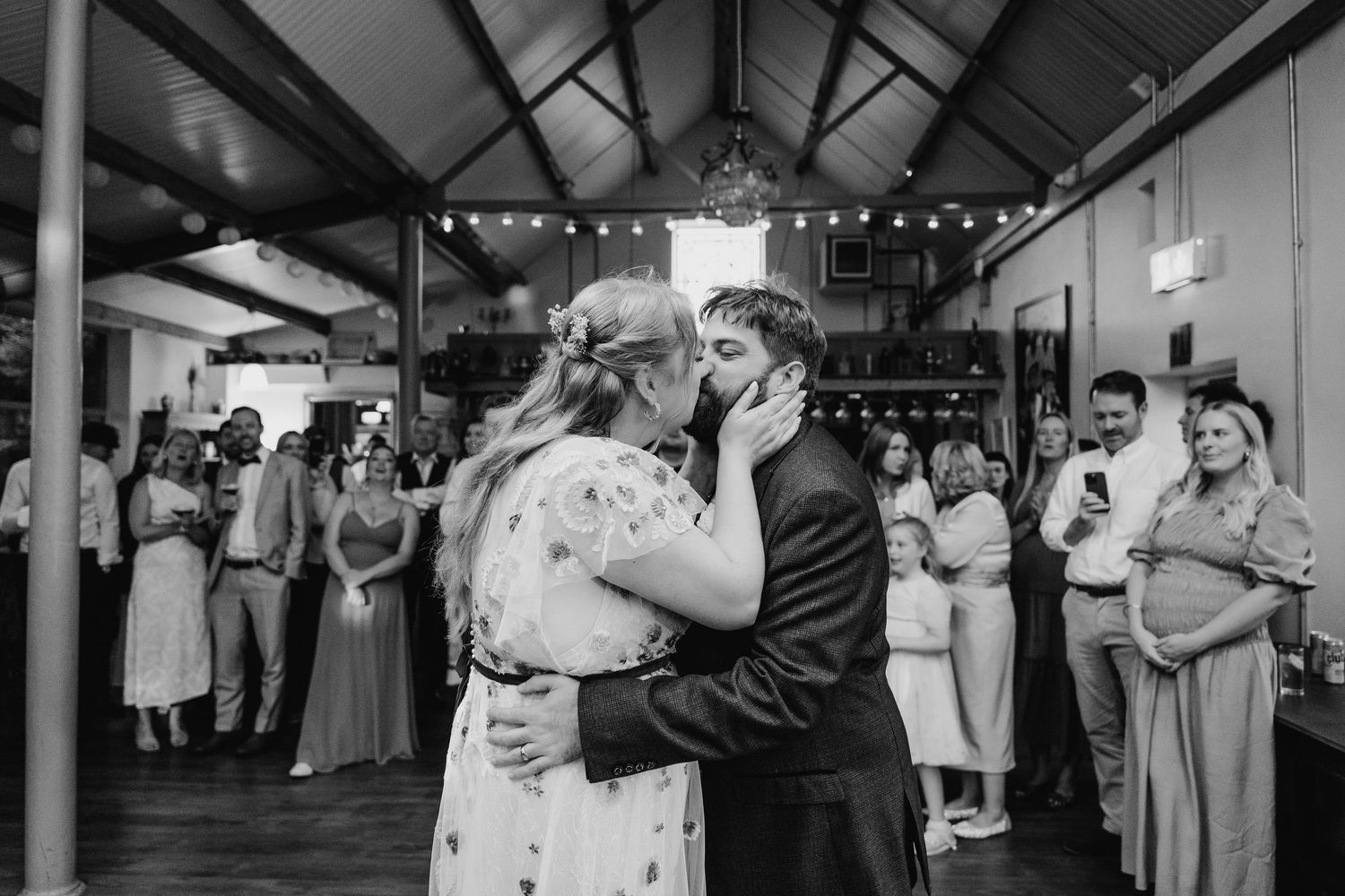 Wedding guests mingling and socializing under string lights in a rustic indoor reception venue. . Village Barn Tyrrellspass wedding photogra