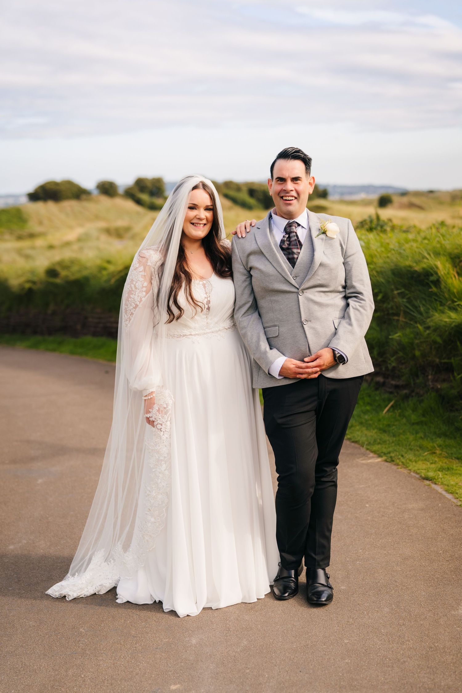Newlyweds pose together outdoors on a scenic country path in romantic wedding attire. Portmarnock Hotel Wedding PHOTOGRAPHER Dublin