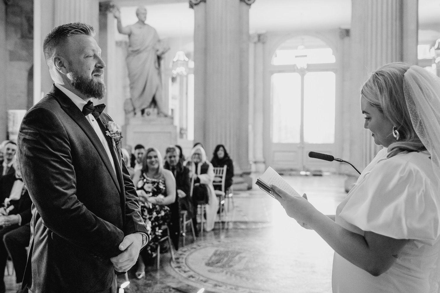 Black and white photo of an intimate wedding ceremony taking place in an elegant room with classical columns and statues. City Hall Dublin P