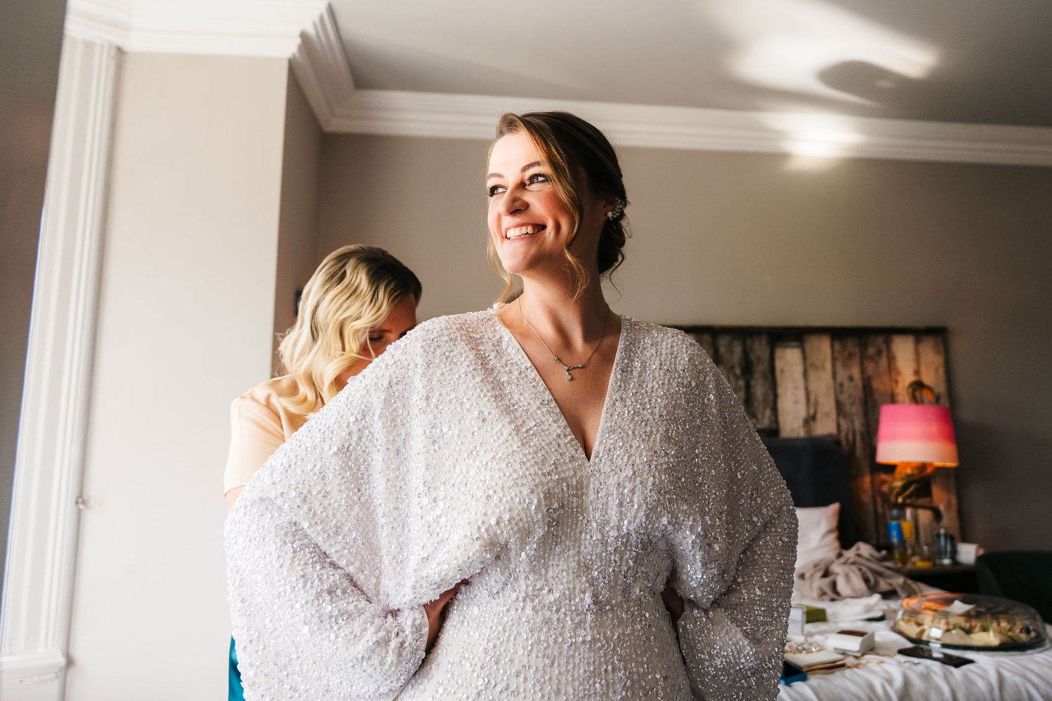A bride wearing a lace long-sleeve wedding dress smiles joyfully during the getting ready portion of her wedding day. House Dublin Wedding P