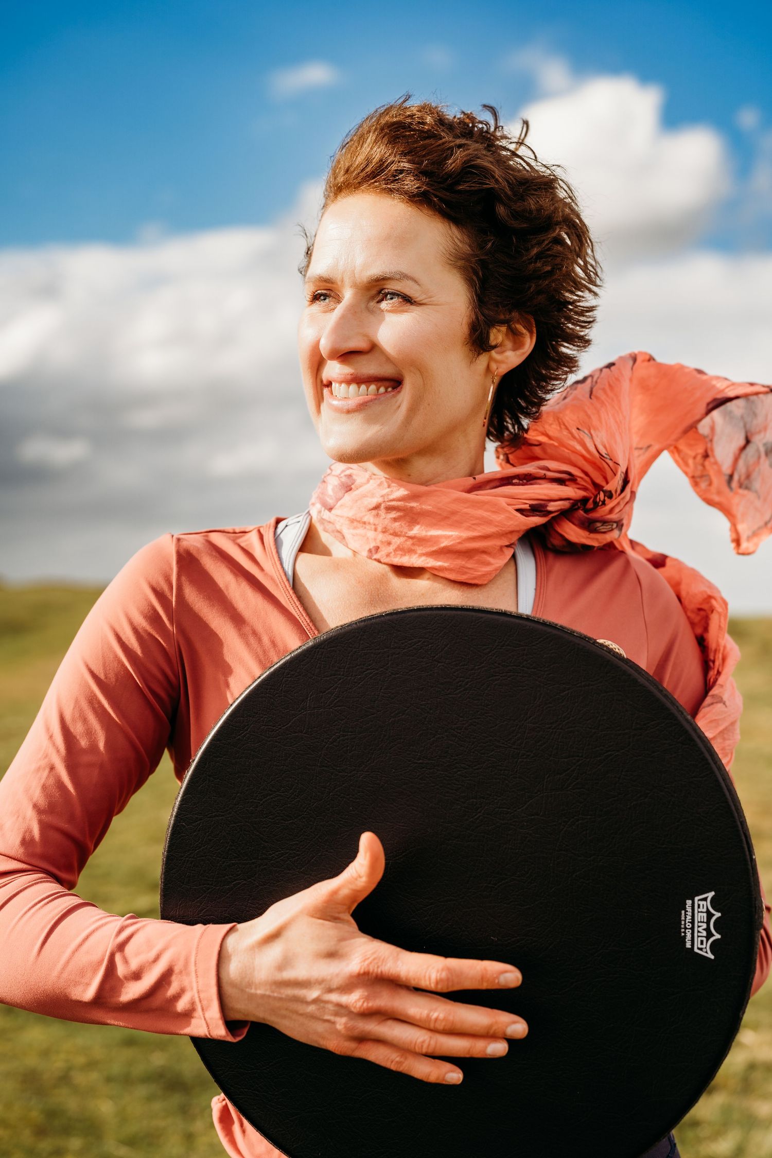 Person in coral jacket smiling while holding black circular exercise balance disc outdoors against blue sky. Portrait PHOTOGRAPHER Dublin