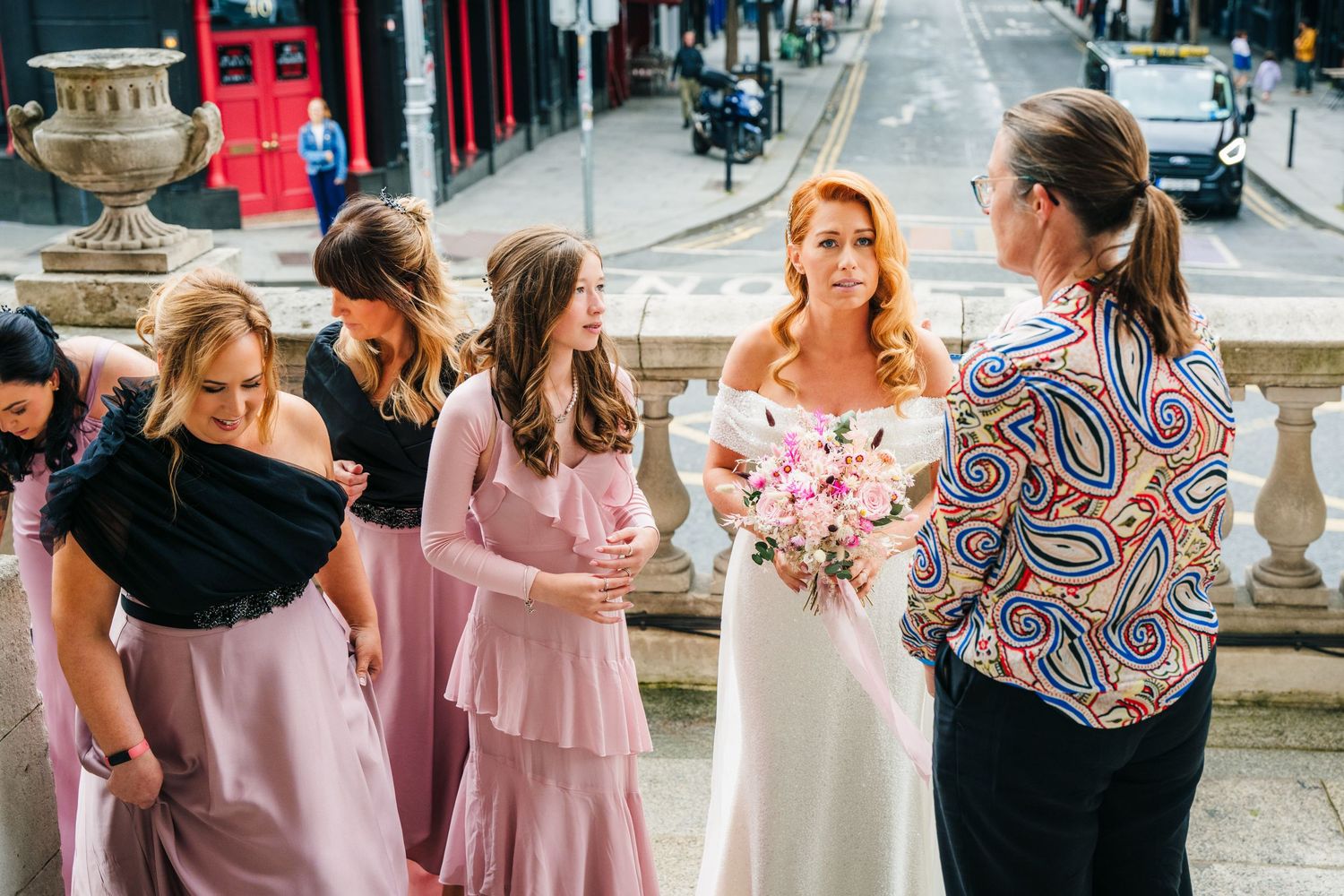 Wedding party in pink dresses gathers outside on a city street.  city hall dublin wedding photos