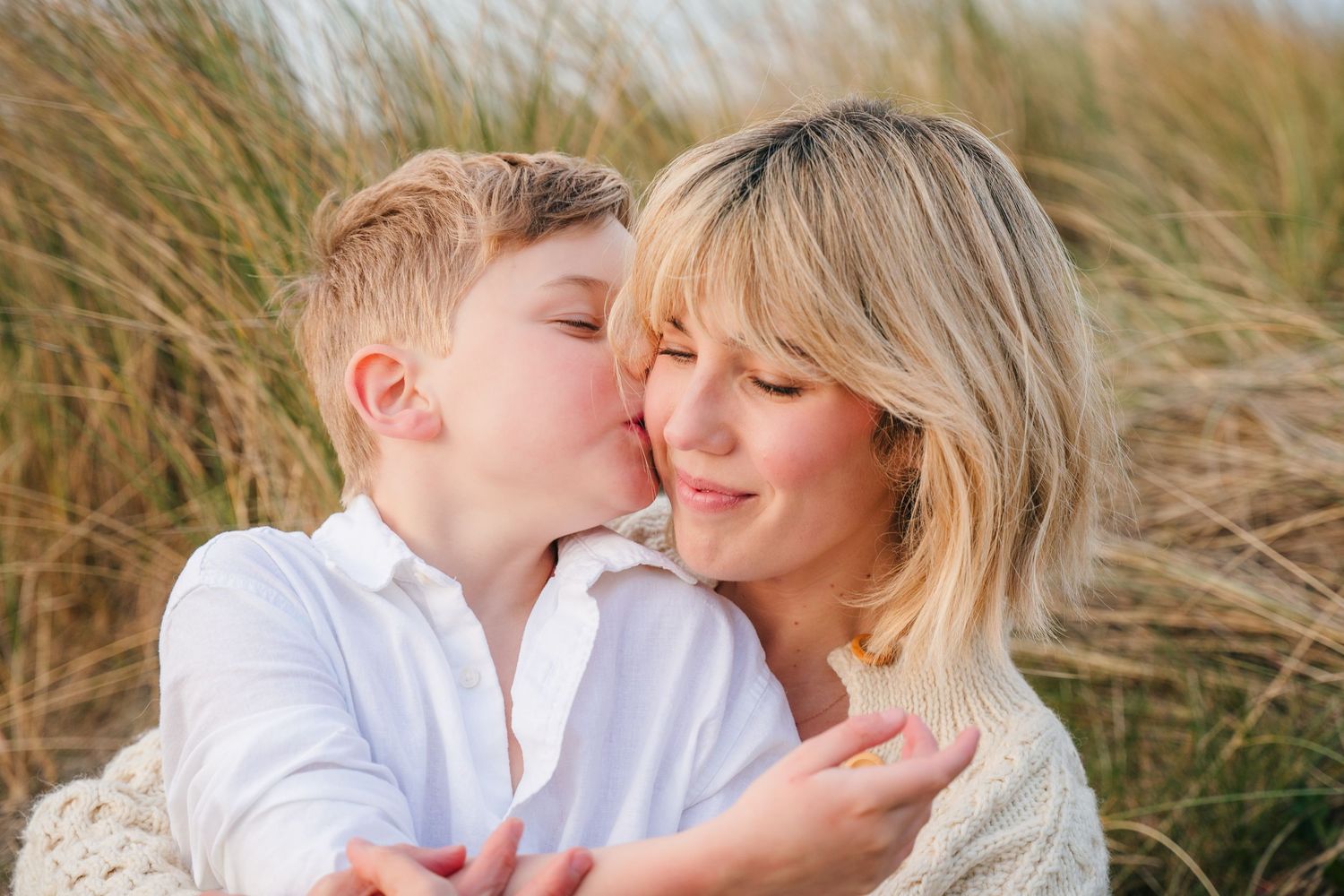A tender moment shared between parent and child amidst tall grass on a sunny day. Family photographer Dublin