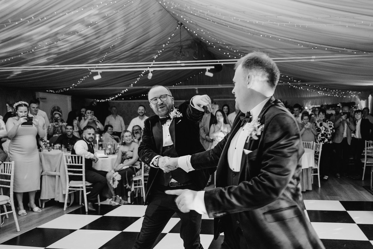 Wedding reception guests dancing on a black and white checkered dance floor under a tent. LGBTQ Ashley Park Wedding Photographer