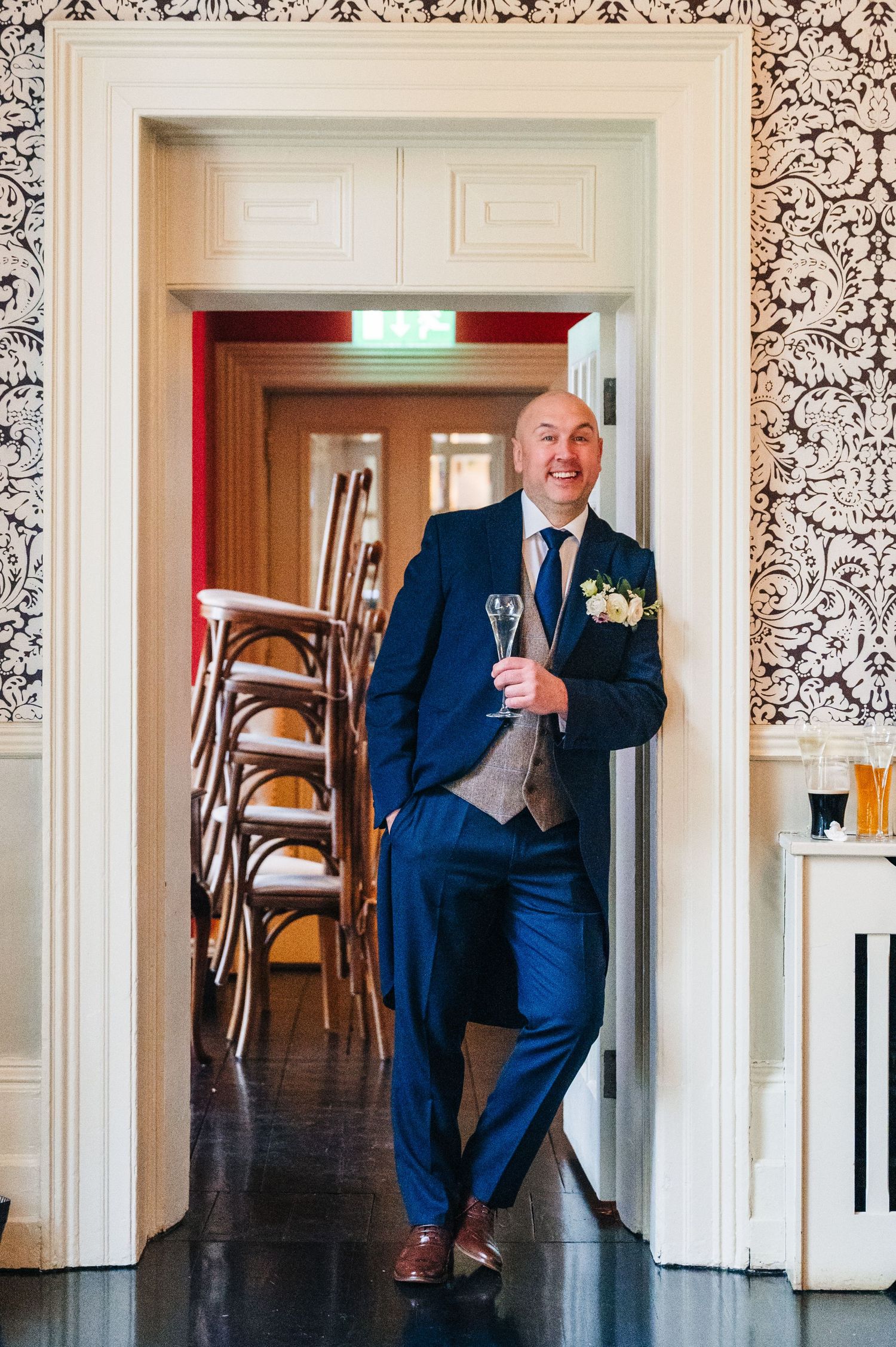 Groomsman in navy suit poses against decorative wallpapered wall in vintage venue.  Virginia Park Lodge Wedding Photographer Cavan Dublin Ir