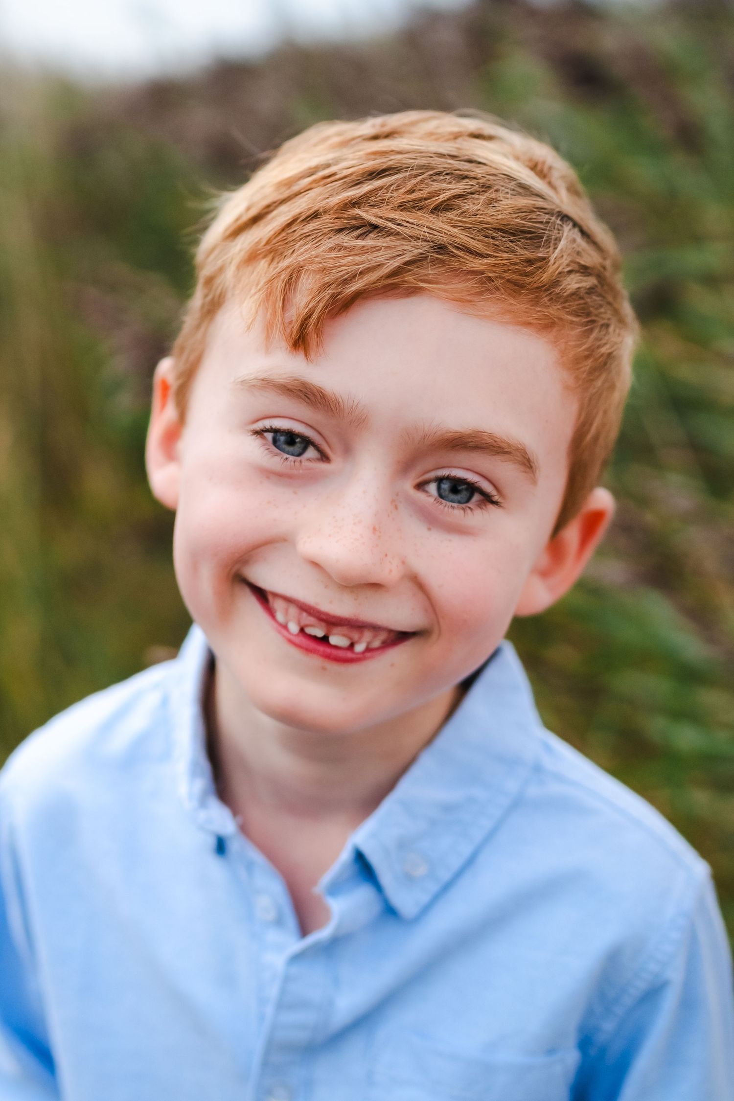 Close-up portrait of a young boy with red hair wearing a light blue collared shirt outdoors.  Family photographer Dublin Ireland
