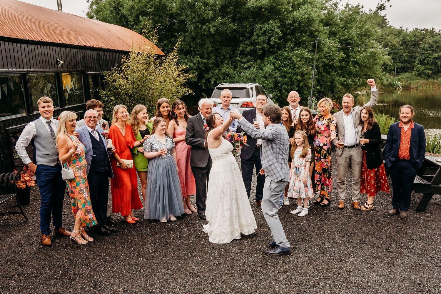 Large group of wedding guests gathered outside a rustic barn venue for a group photo. Wedding photographer Dublin