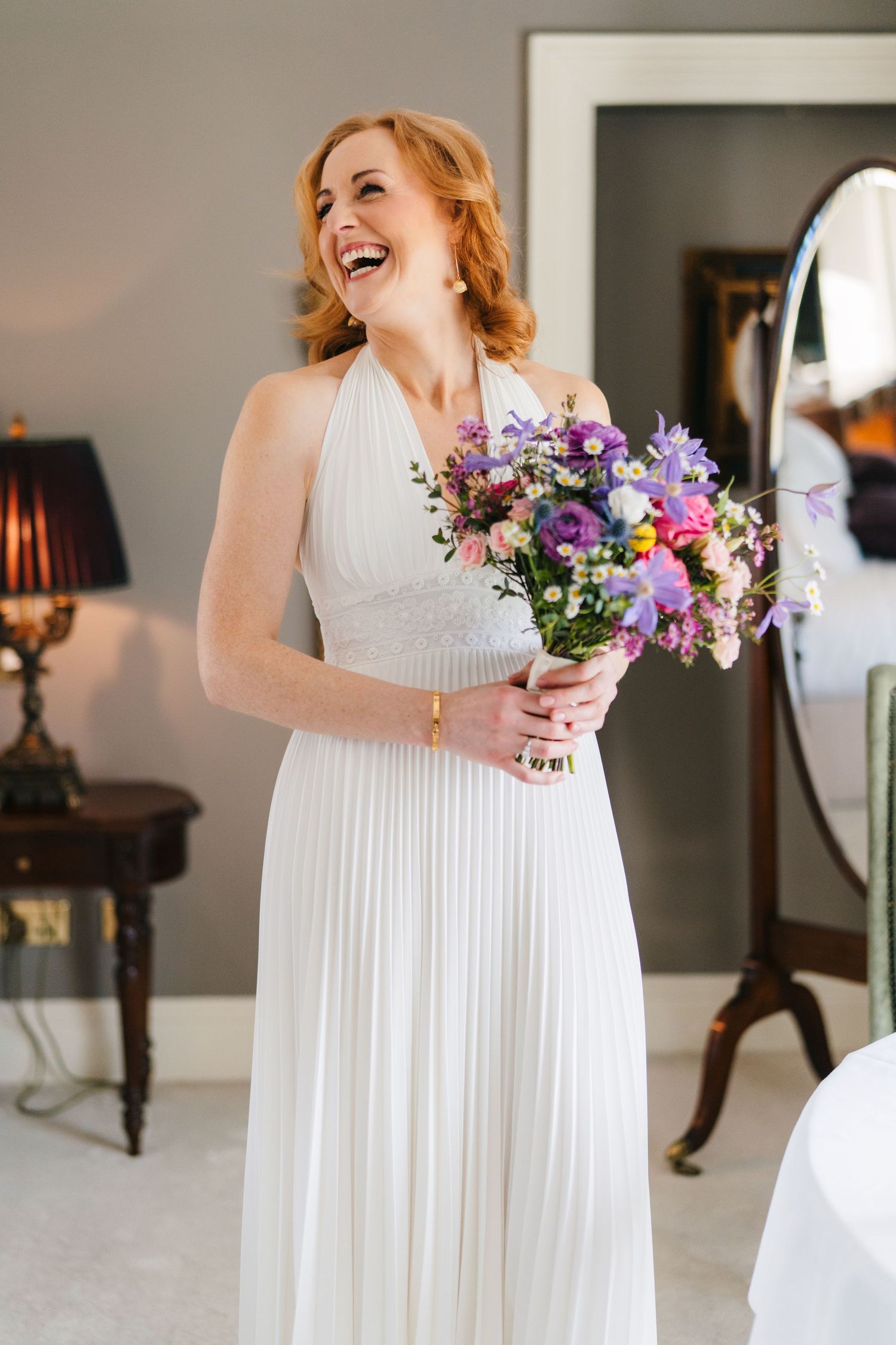 A person in a flowing white wedding dress holds a vibrant purple and pink floral bouquet while laughing joyfully. wedding photographer dubli