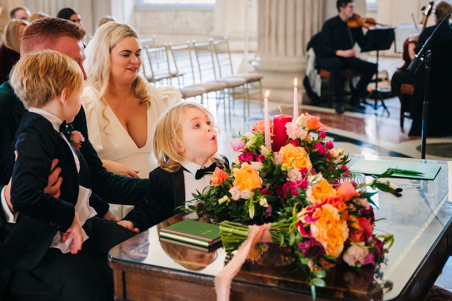 Wedding party gathered around a piano with vibrant floral arrangements. Wedding photographer dublin