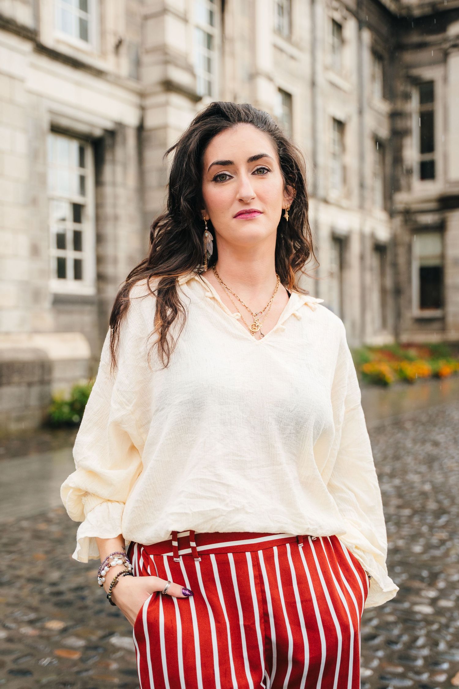 Fashion model wearing white blouse and red striped pants poses against historic stone building exterior. professional headshots dublin