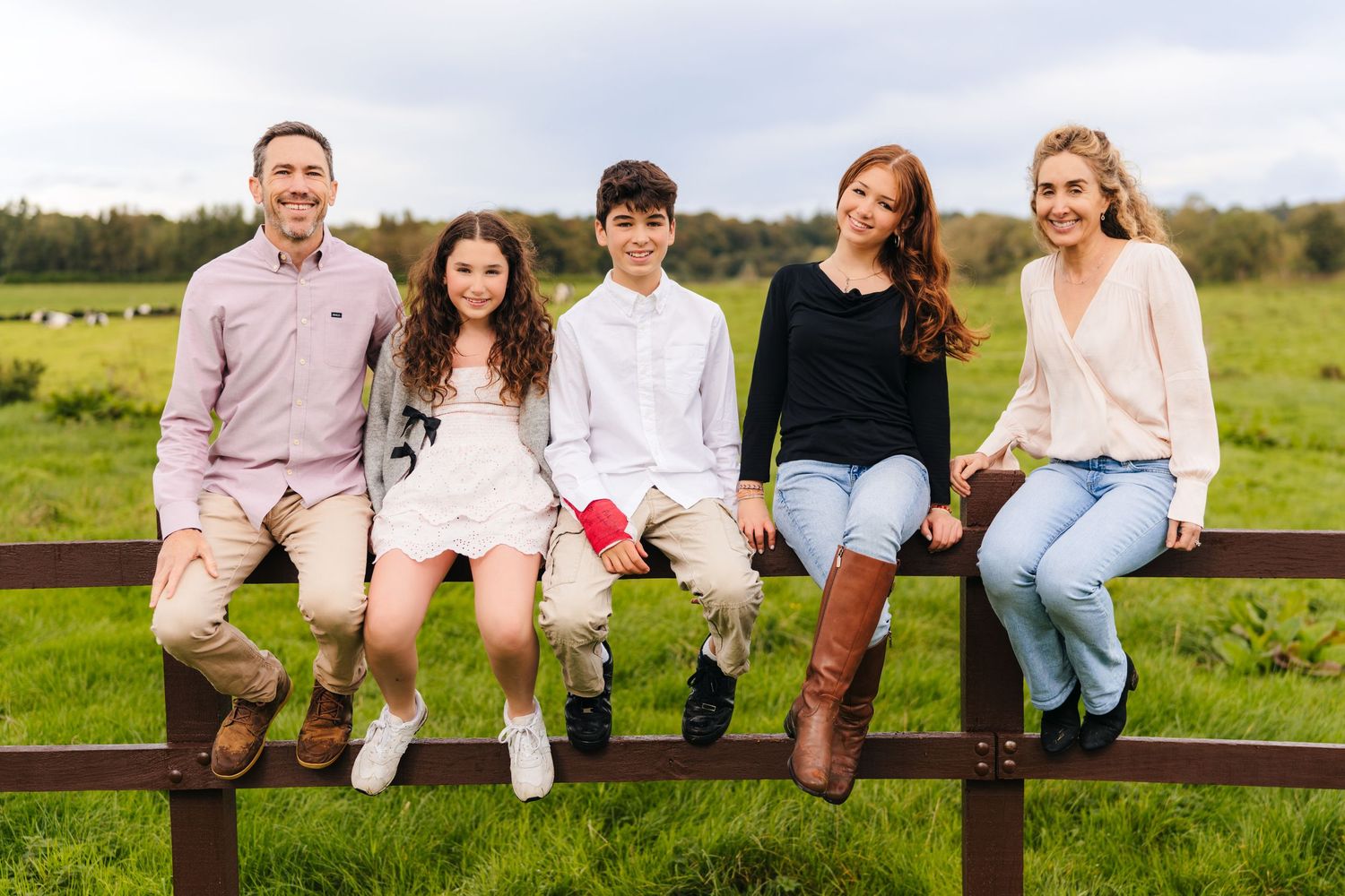 Family members sitting together on a wooden fence in a grassy field. BEctive abbey family photographer dublin