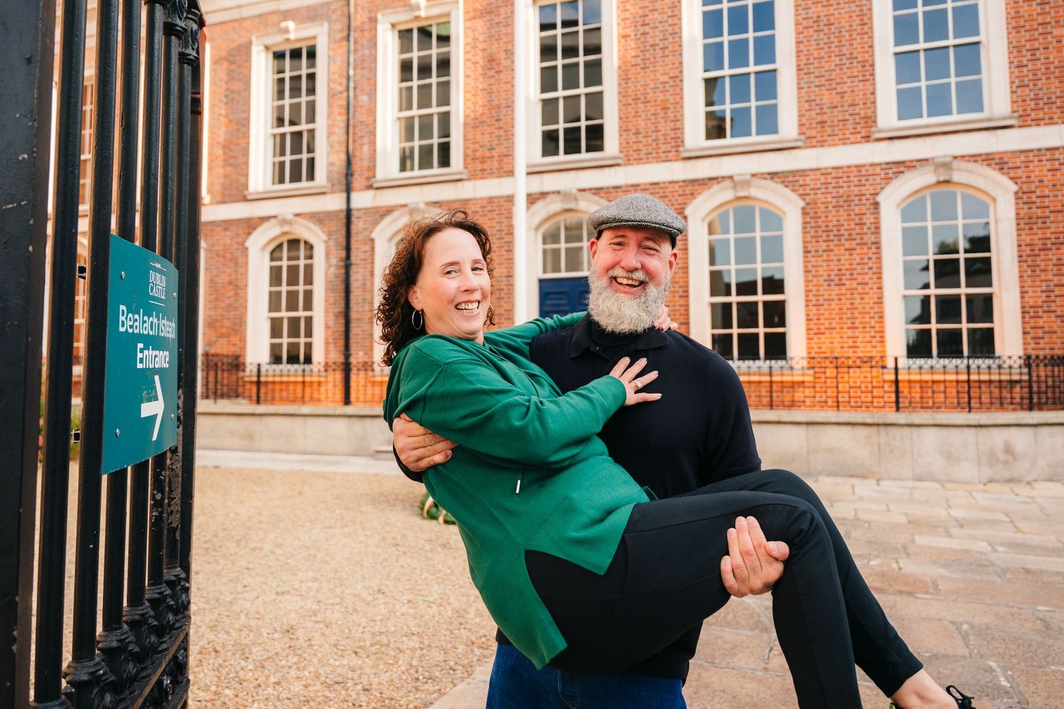 A couple shares a playful moment outside a grand brick building with large windows. PHOTOGRAPHER Dublin PHOTOGRAPHER Dublin ireland