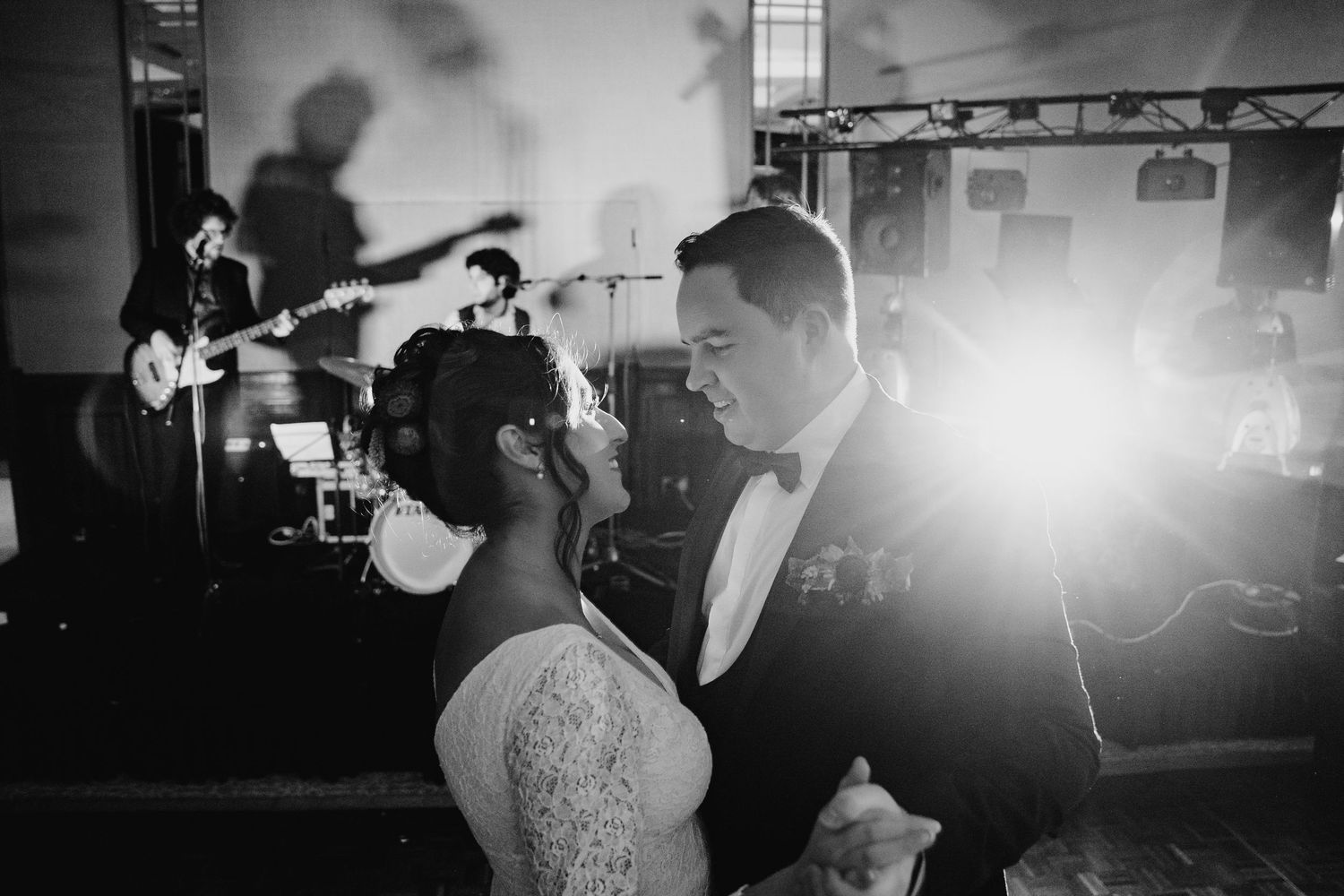 Black and white photo of newlyweds sharing a dance at their wedding reception while a band performs in the background.