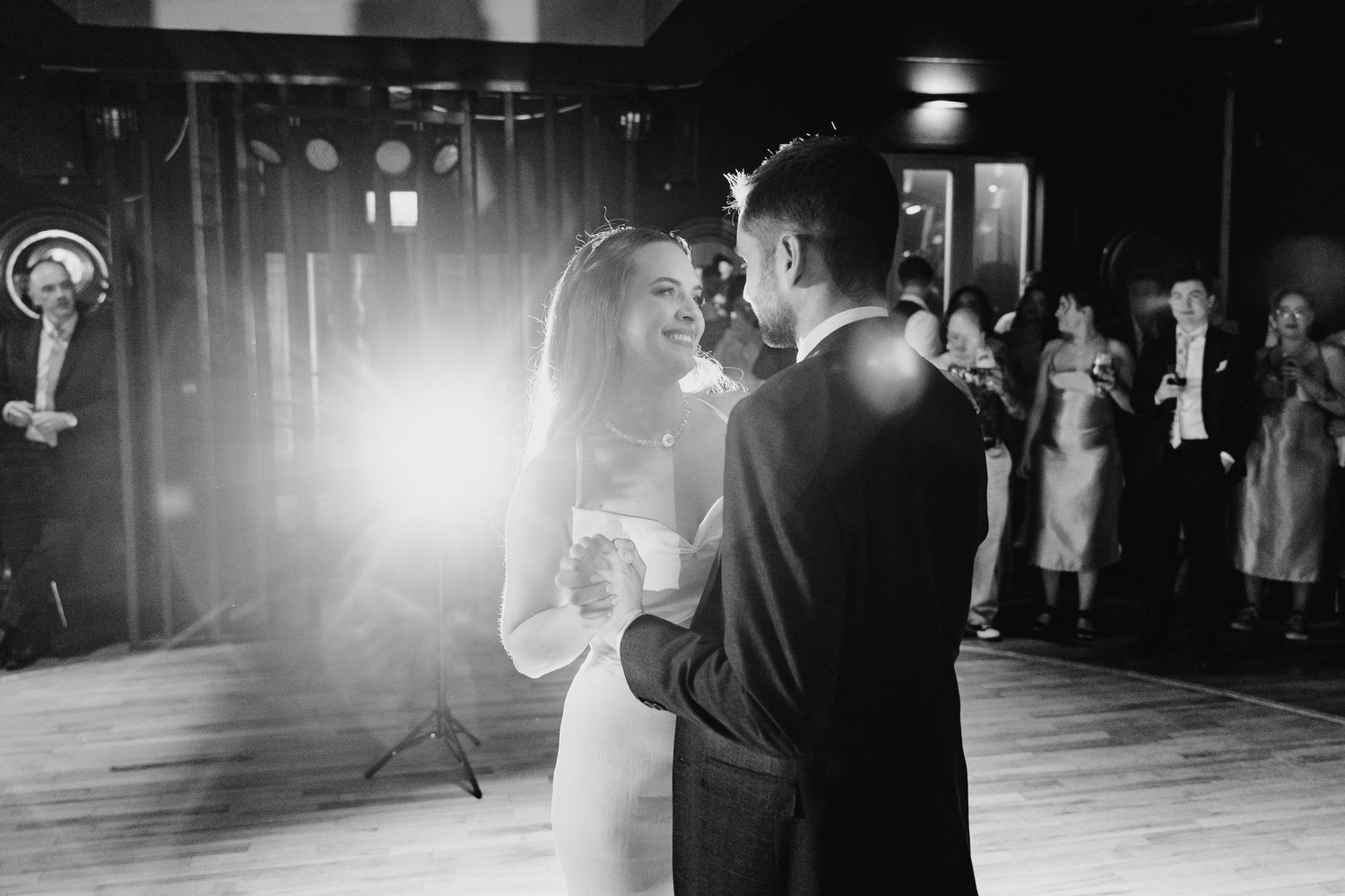 A couple shares their first dance as newlyweds on an illuminated dance floor with guests watching in the background.