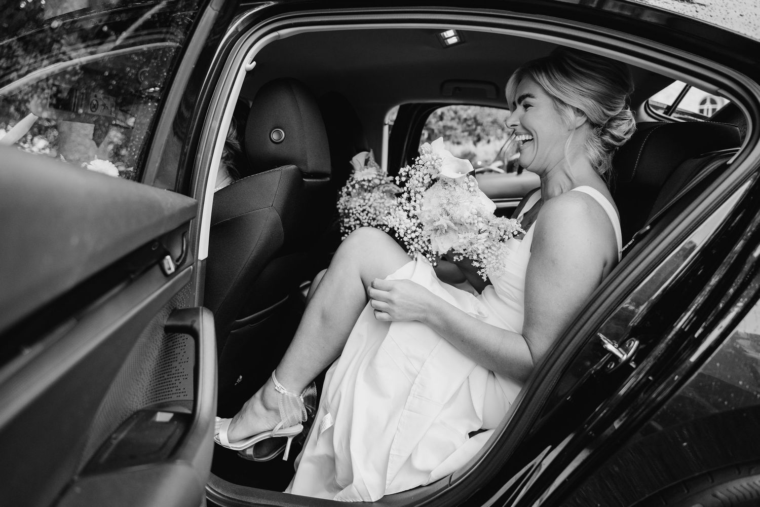 Black and white image of bride in classic car with elegant floral bouquet. The Dean Dublin Wedding Photographer