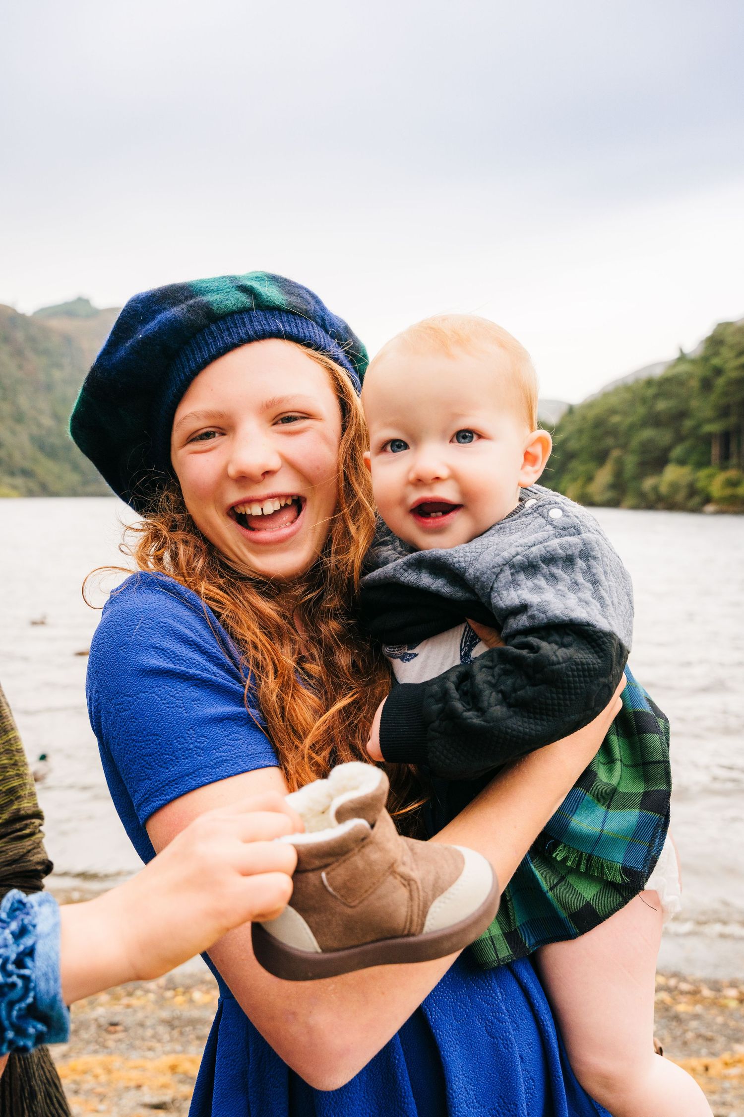 A family shares loving embraces and laughter while wearing blue and plaid clothing by a scenic lake.Family photogrAPHER DUBLIN