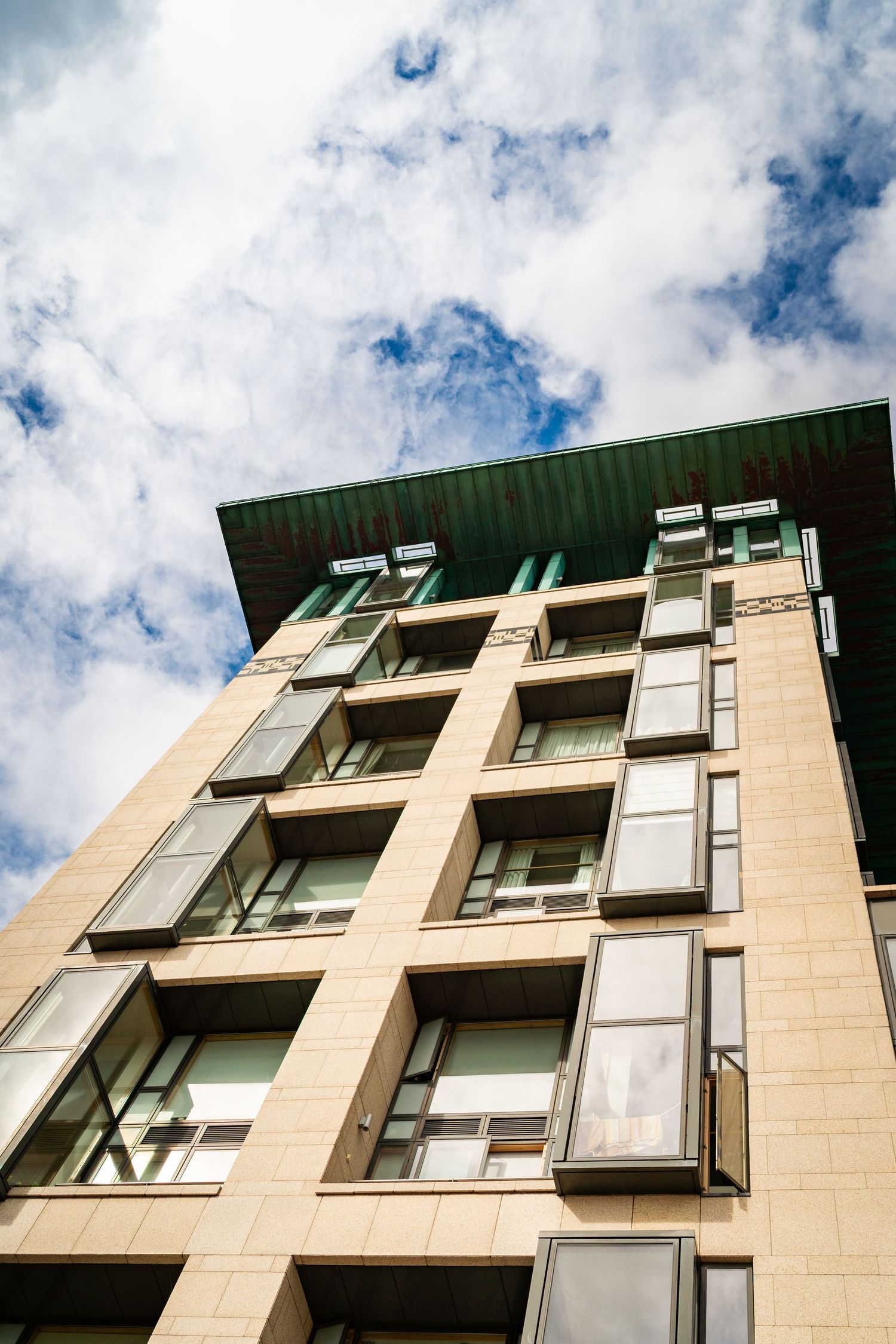 Modern apartment building facade with light-colored stone and glass balconies against a cloudy sky. Couple's Photoshoot PHOTOGRAPHER Dublin