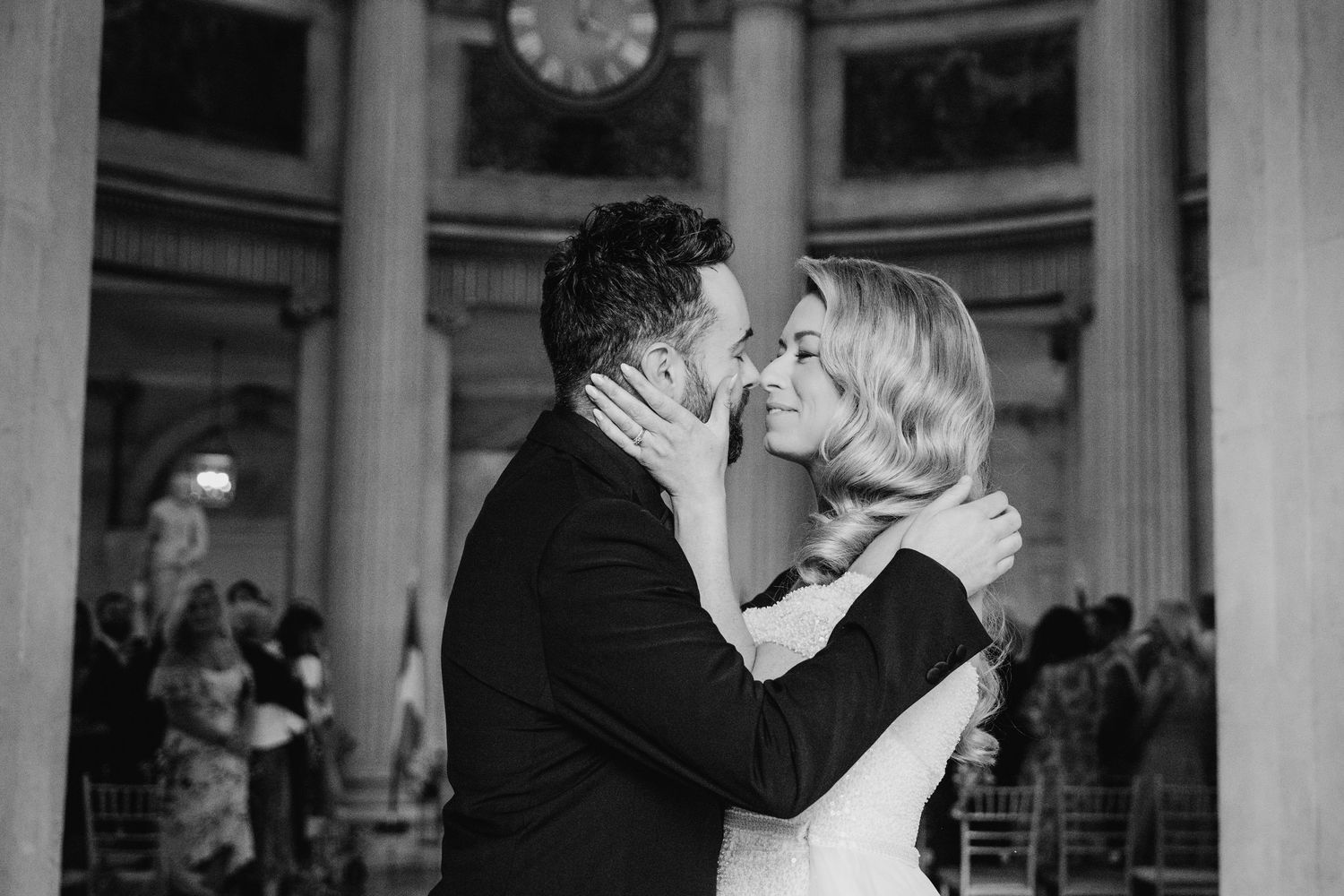 A couple shares a romantic dance embrace in an elegant columned hall during what appears to be their wedding celebration.