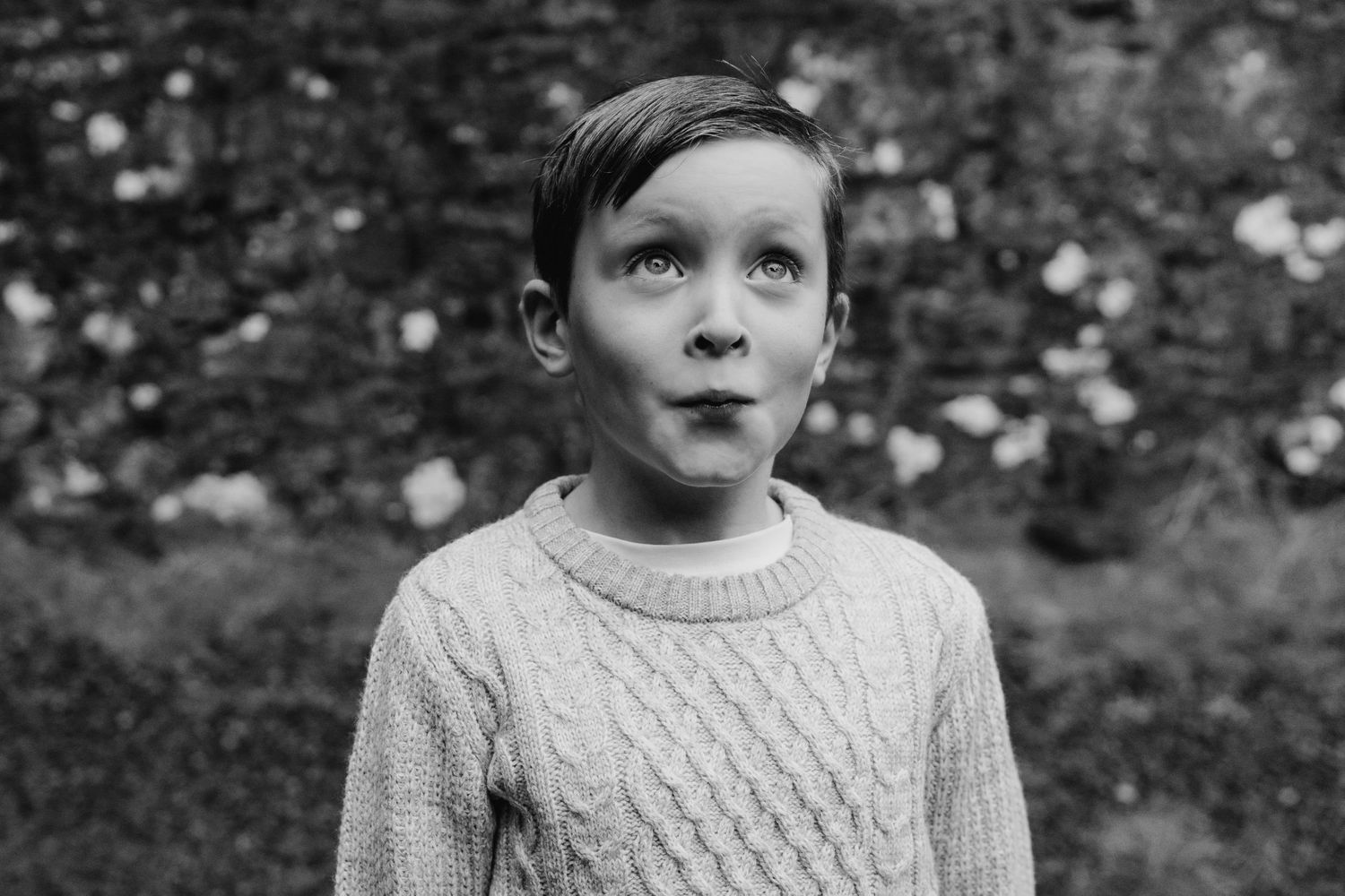 Black and white portrait photo of small child wearing a knitted sweater and looking at camera with serious expression. family PHOTOGRAPHER D