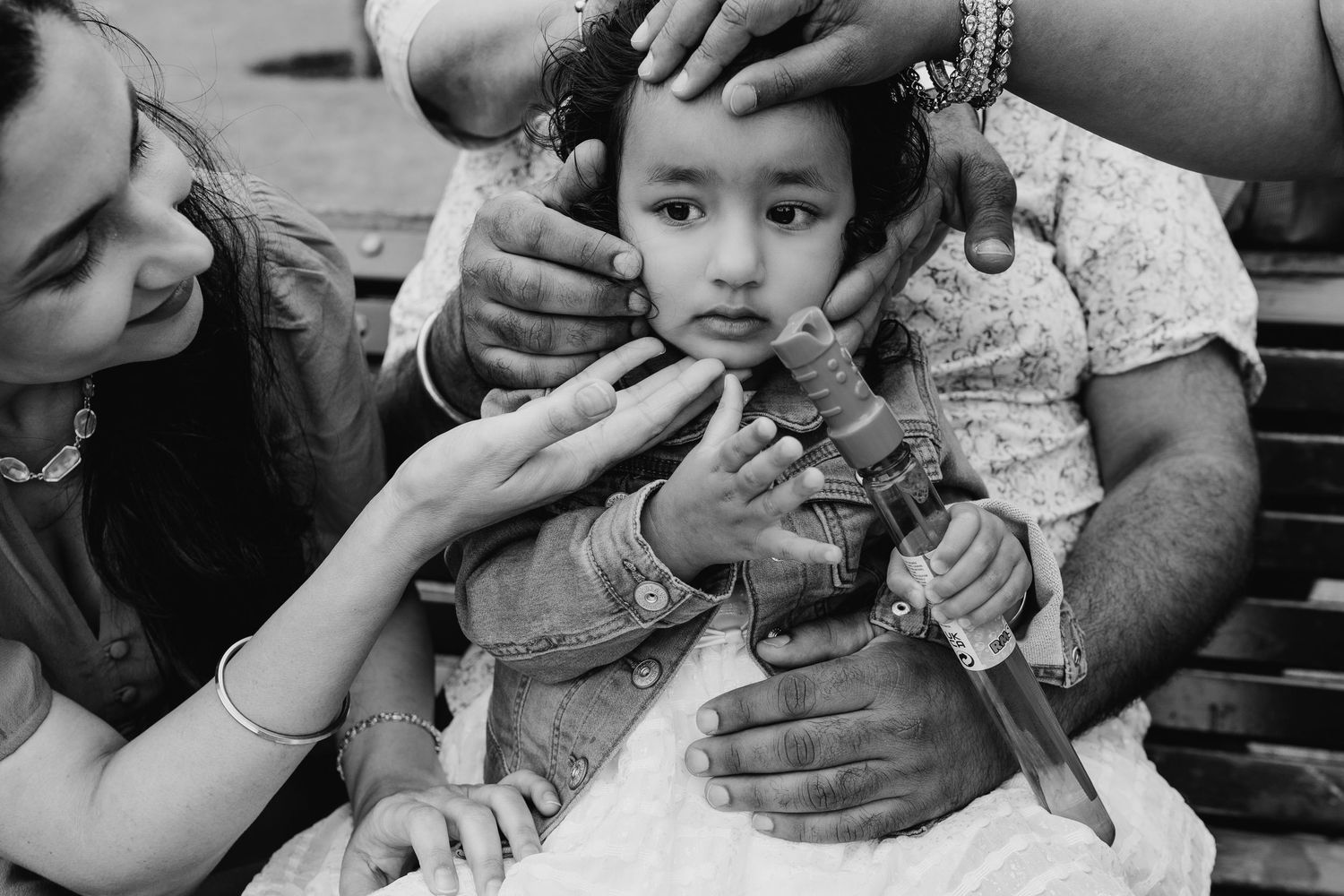 A black and white photograph showing hands administering medication to a child during a medical procedure. family PHOTOGRAPHER Dublin