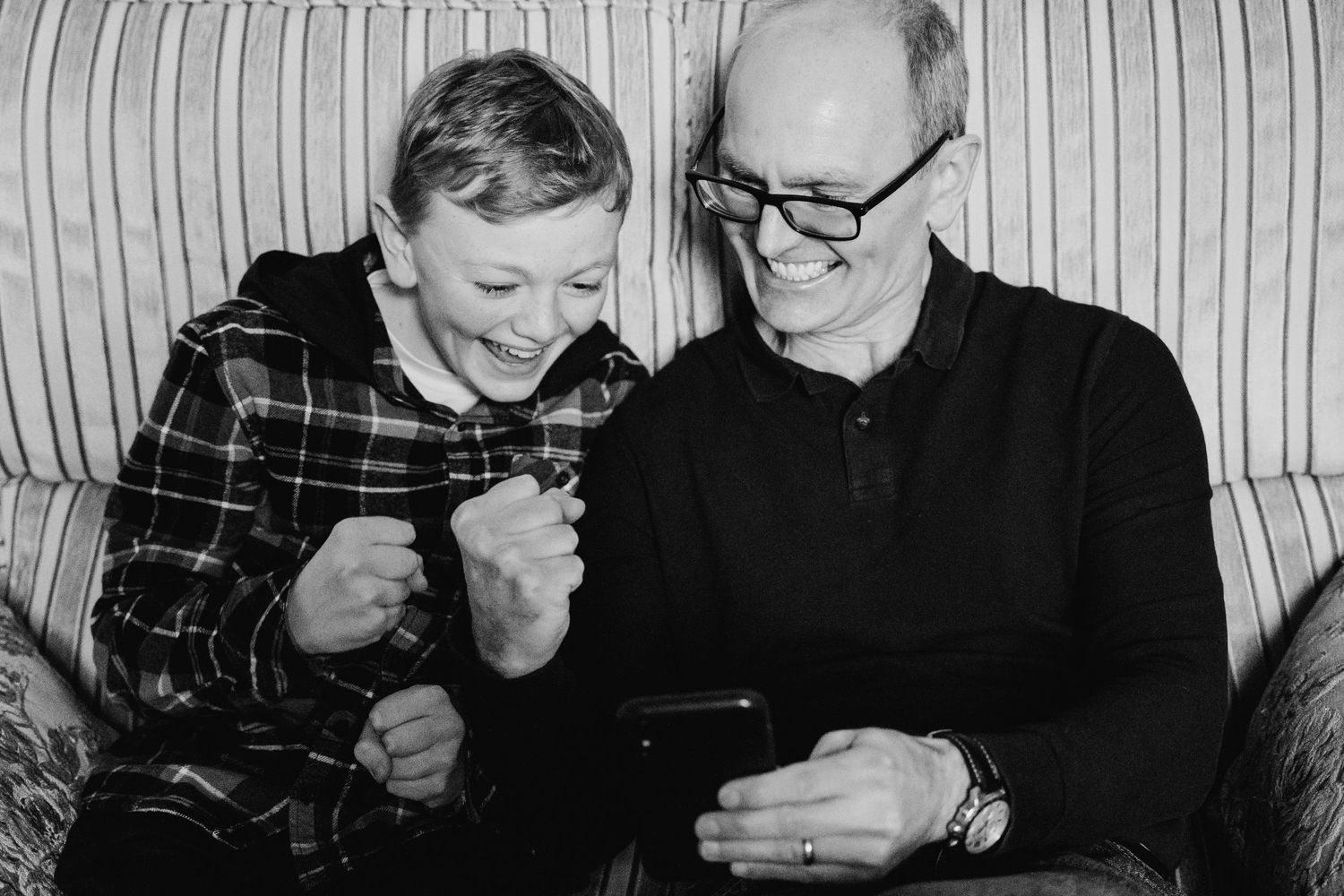 A child and an older man sit together on a couch looking at a device while sharing a joyful moment. family PHOTOGRAPHER Dublin