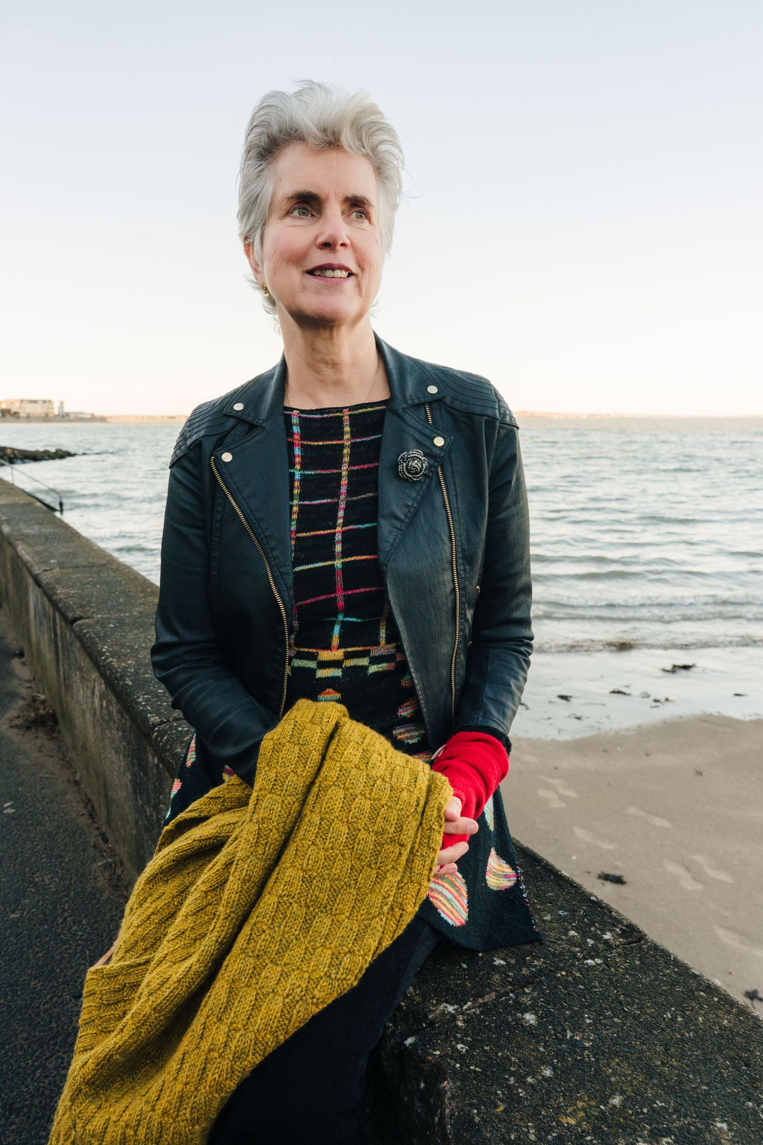 A figure in a leather jacket and yellow shawl stands on a beach at sunset. professional headshots branding photographer dublin ireland