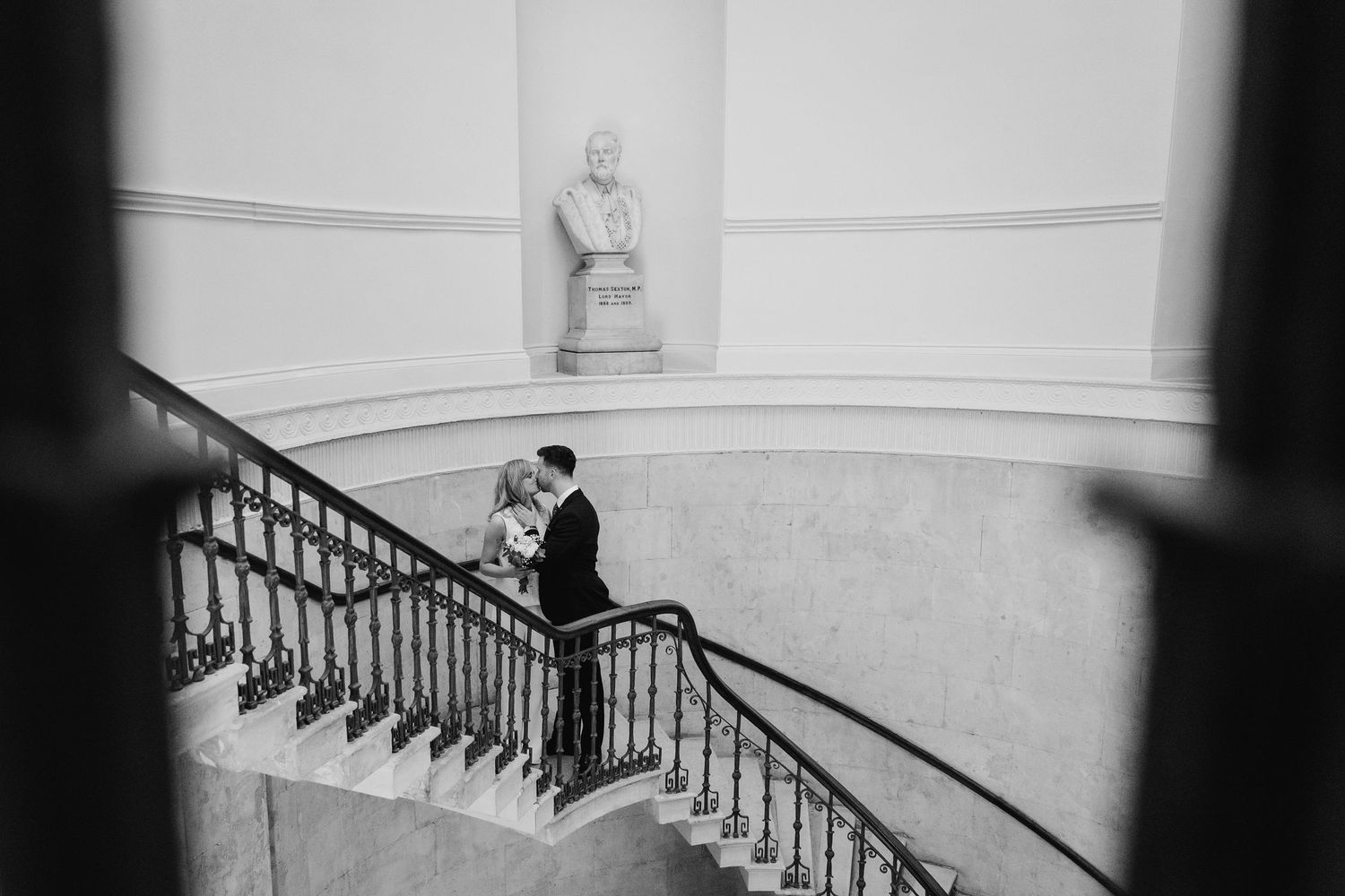 Guests seated at a grand staircase inside an ornate building with white pillars and classical architecture. City Hall Dublin wedding photogr
