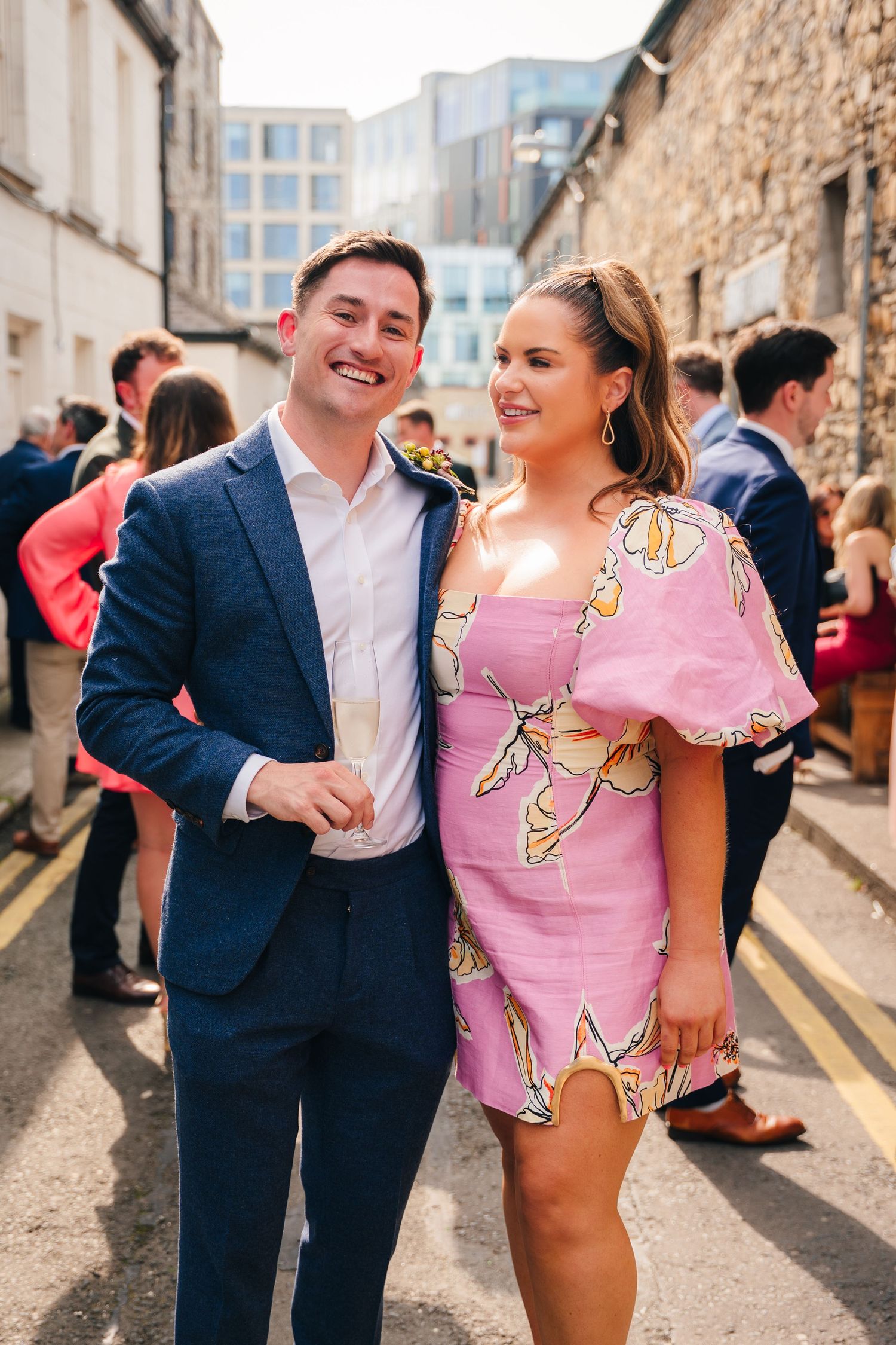 Guests at an outdoor event with stone walls and urban buildings in the background. Same sex wedding PHOTOGRAPHER Dublin