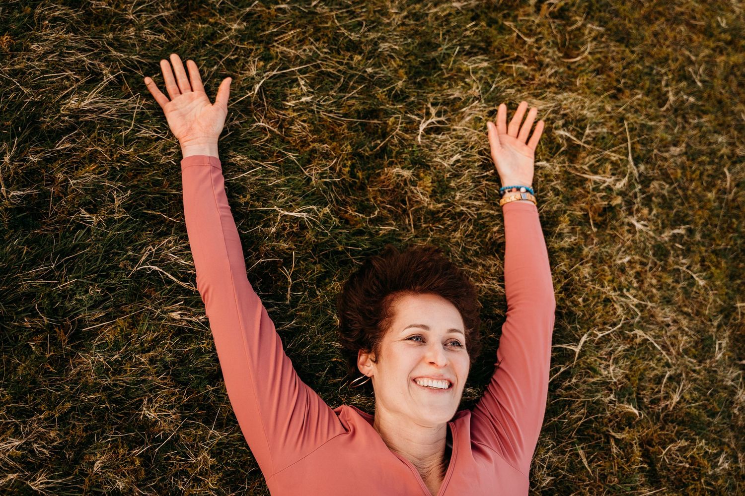 Person in coral sweater sits in autumn leaves with raised arms against fall foliage background. Portrait PHOTOGRAPHER Dublin