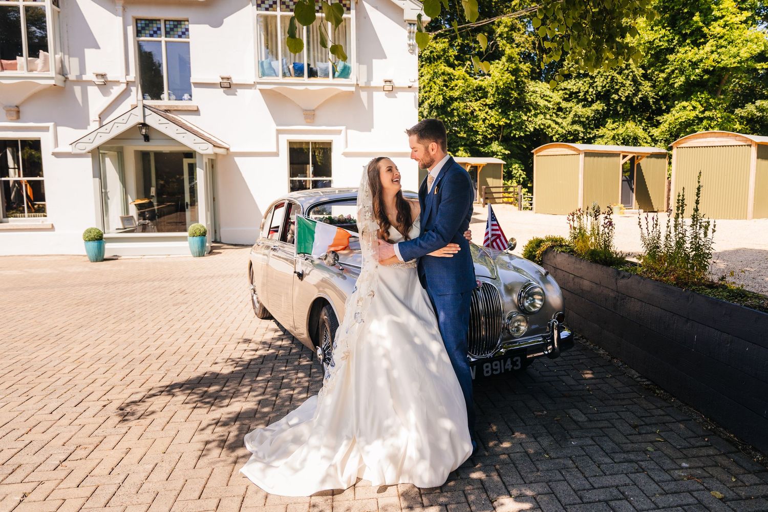 Poulaphouca Wedding photogA classic vintage car parked on brick pavement outside an elegant white building creates a romantic wedding scene.