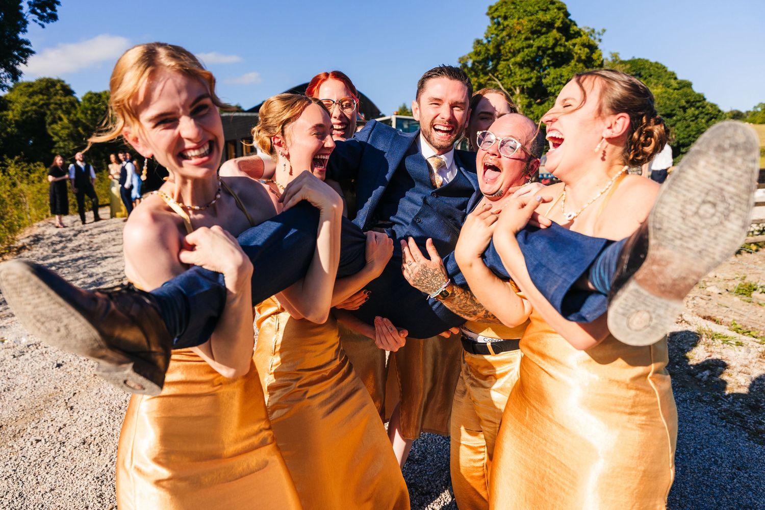 Poulaphouca Wedding photographer wicklow  Wedding party in matching gold dresses and navy suits laughing together on a gravel path outdoors.